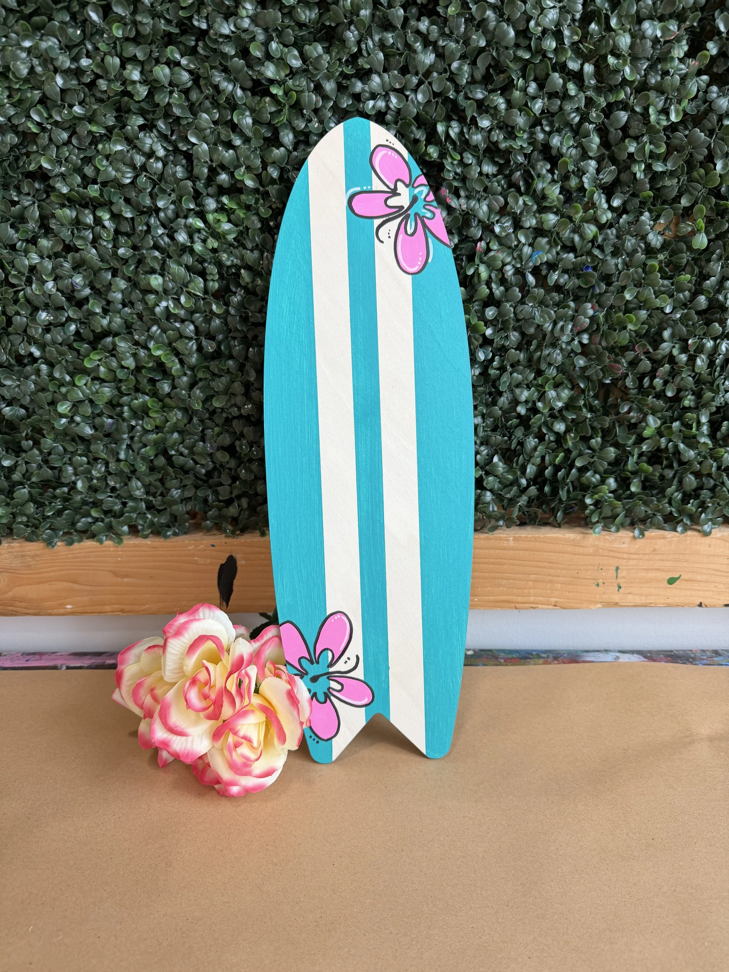 Turquoise painted mini surf board with pink hibiscus flowers painted on it.