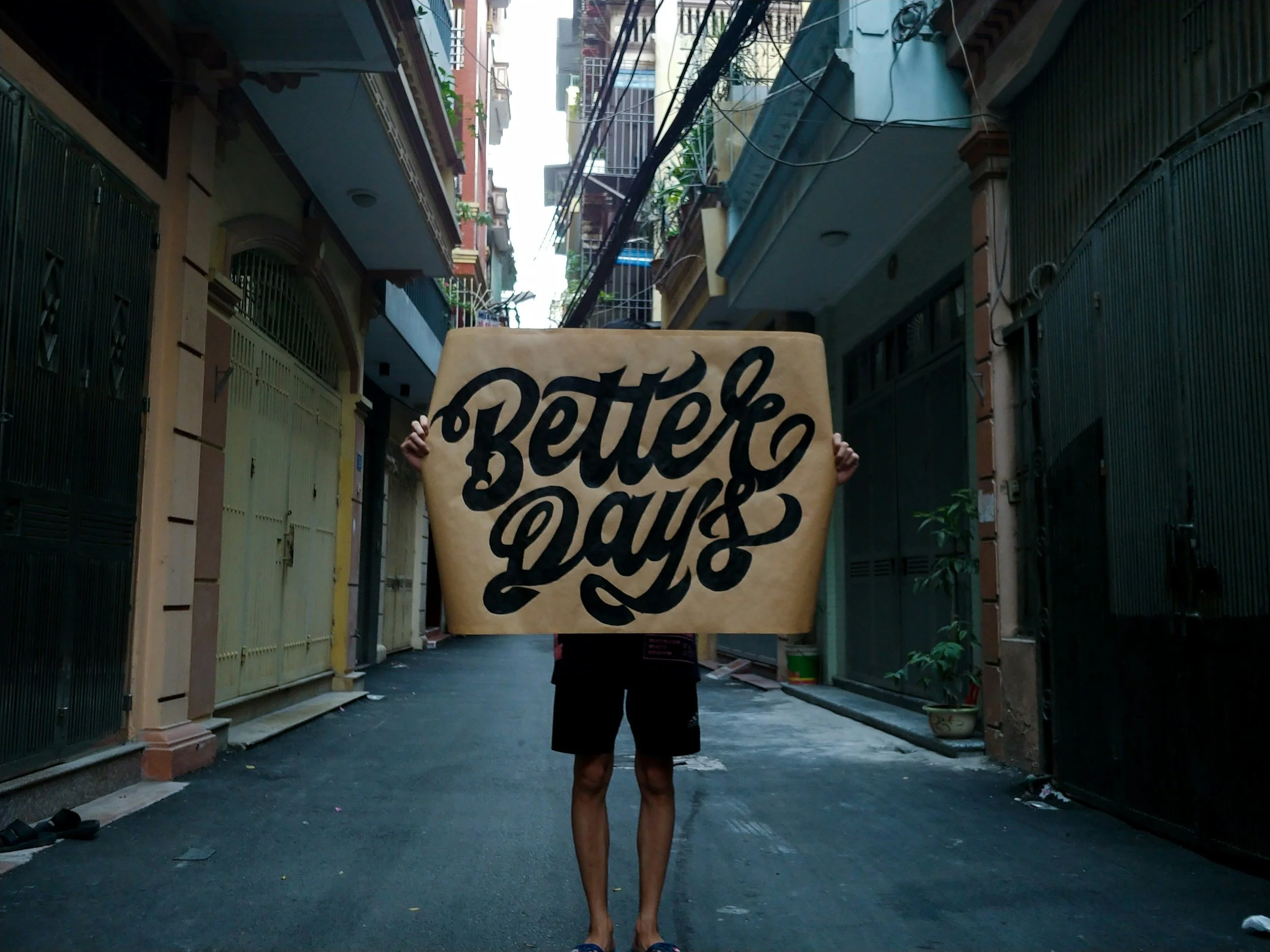 Person holding a large sign on a street in an urban area, with buildings and power lines overhead.