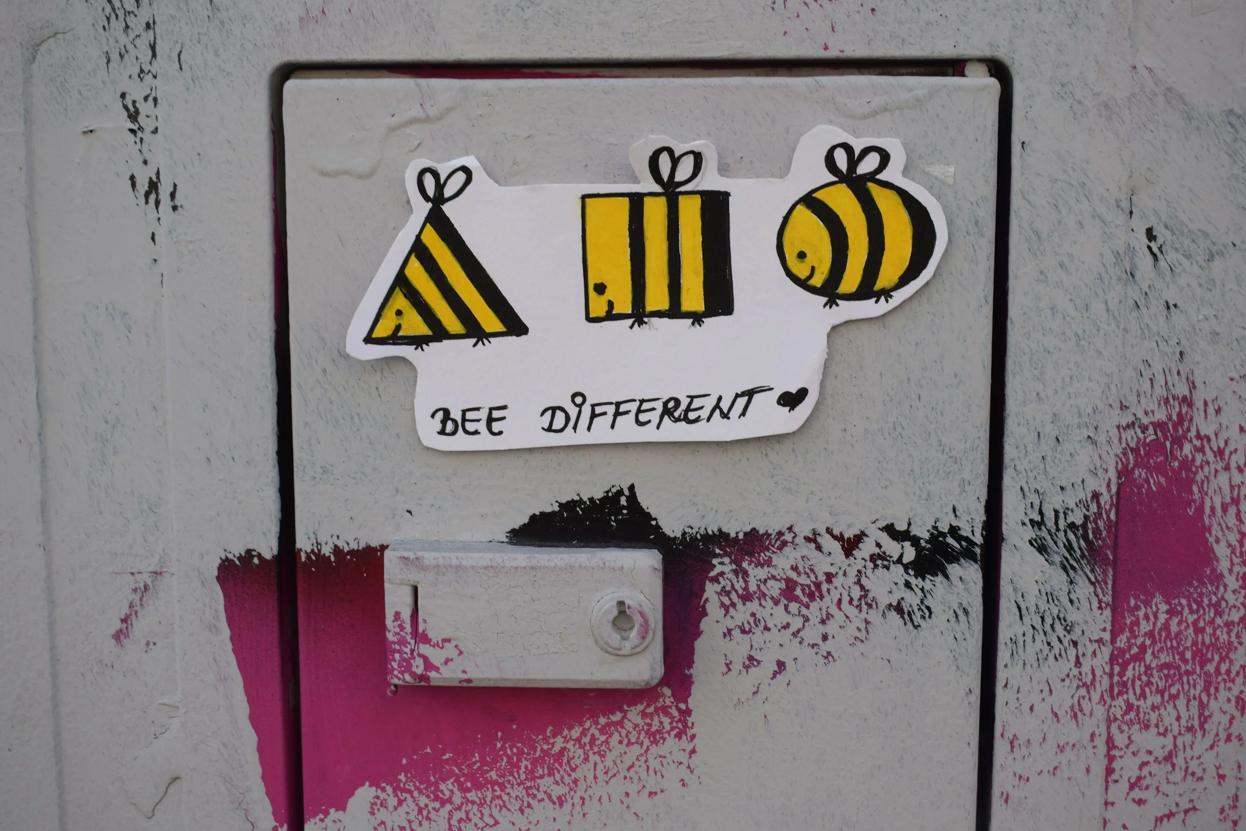 Sticker of three bees with the words 'Bee Different' on a vent cover on a painted wall.
