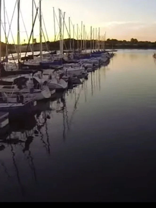 Sailboats docked along a peaceful waterway at sunset with reflections on the water.