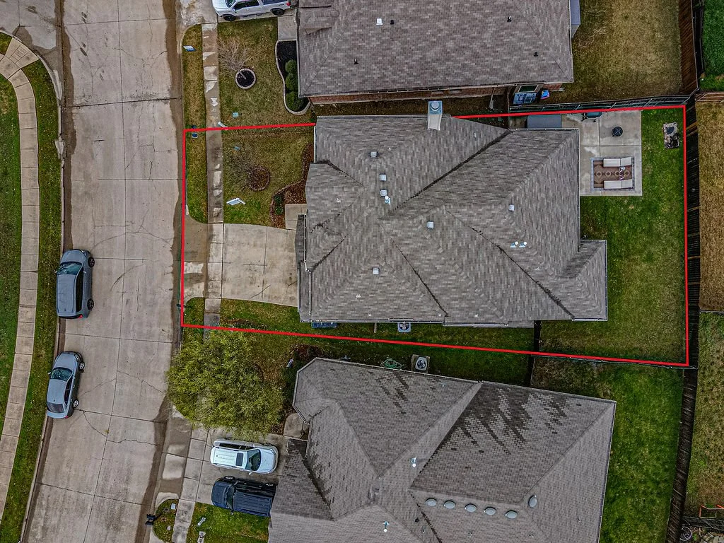 Aerial view of a house and backyard, with a red boundary line marking the yard's perimeter, adjacent to a street with parked cars.