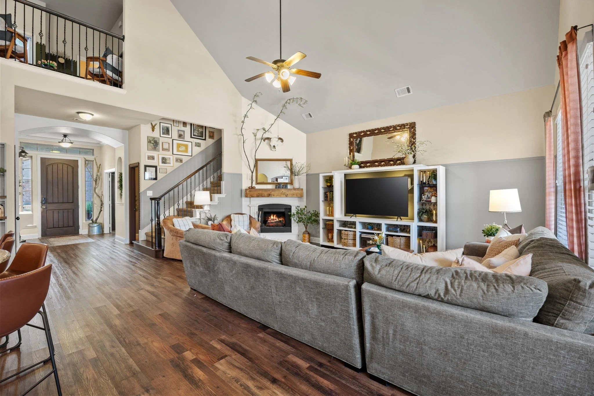 Spacious living room with gray sofa, fireplace, large flat-screen TV, and wooden floors
