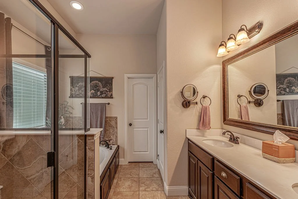 Bathroom with a glass shower, bathtub, and a large mirror above a double vanity with dark wood cabinets, beige countertop, and pink hand towel.