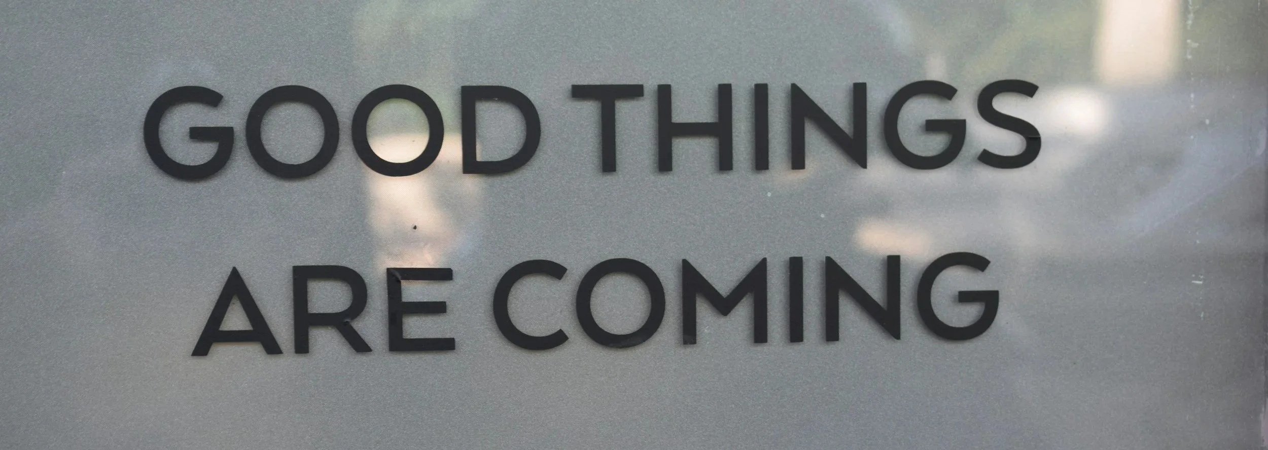Sign that reads 'Good Things Are Coming' in black letters on a reflective silver background.