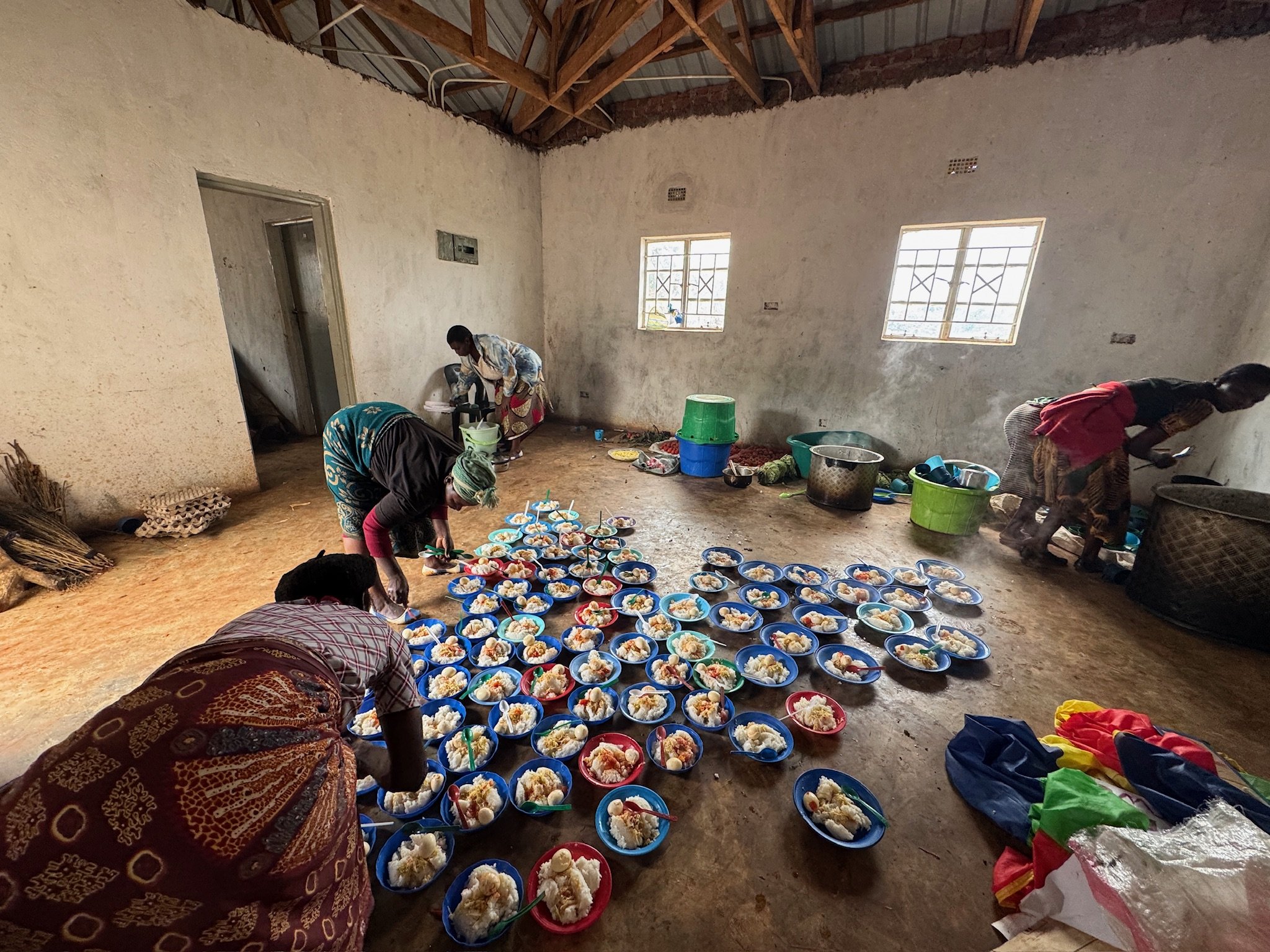 People preparing and arranging plates of food in a spacious room with unfinished walls and windows.