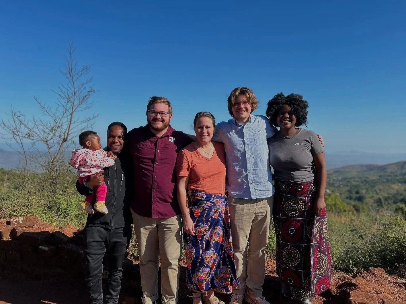 Smiling person with curly hair wearing glasses and a striped shirt.