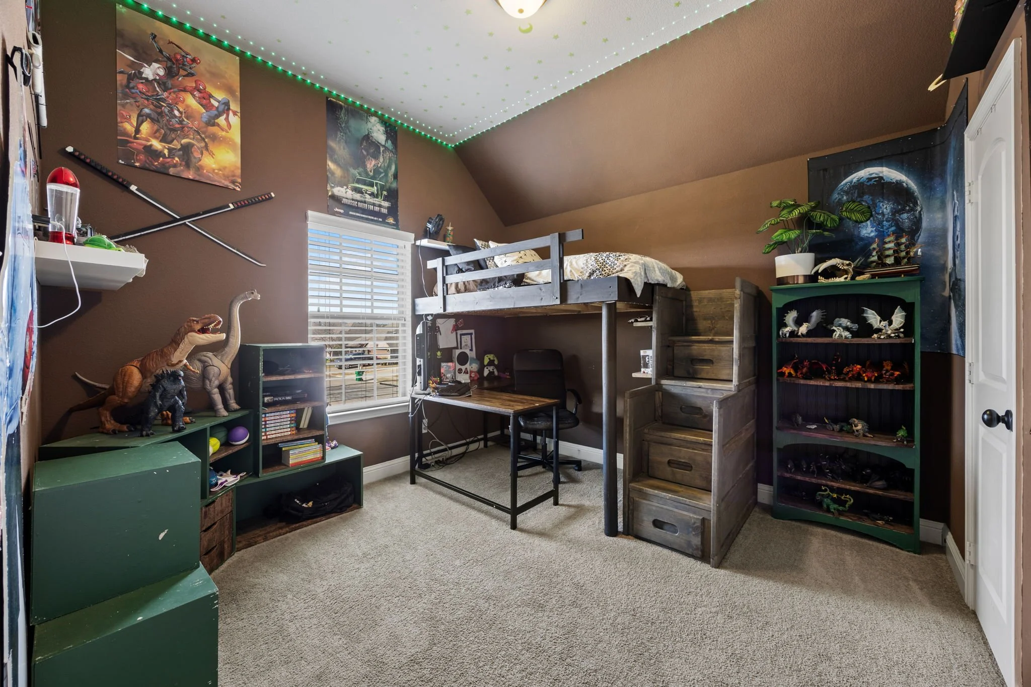 A bedroom with brown walls, a window with blinds, and a sloped ceiling decorated with green LED lights. The room contains a loft bed with a wooden ladder, a desk with a chair underneath, and shelves filled with toys, posters, and decorations. Dinosau