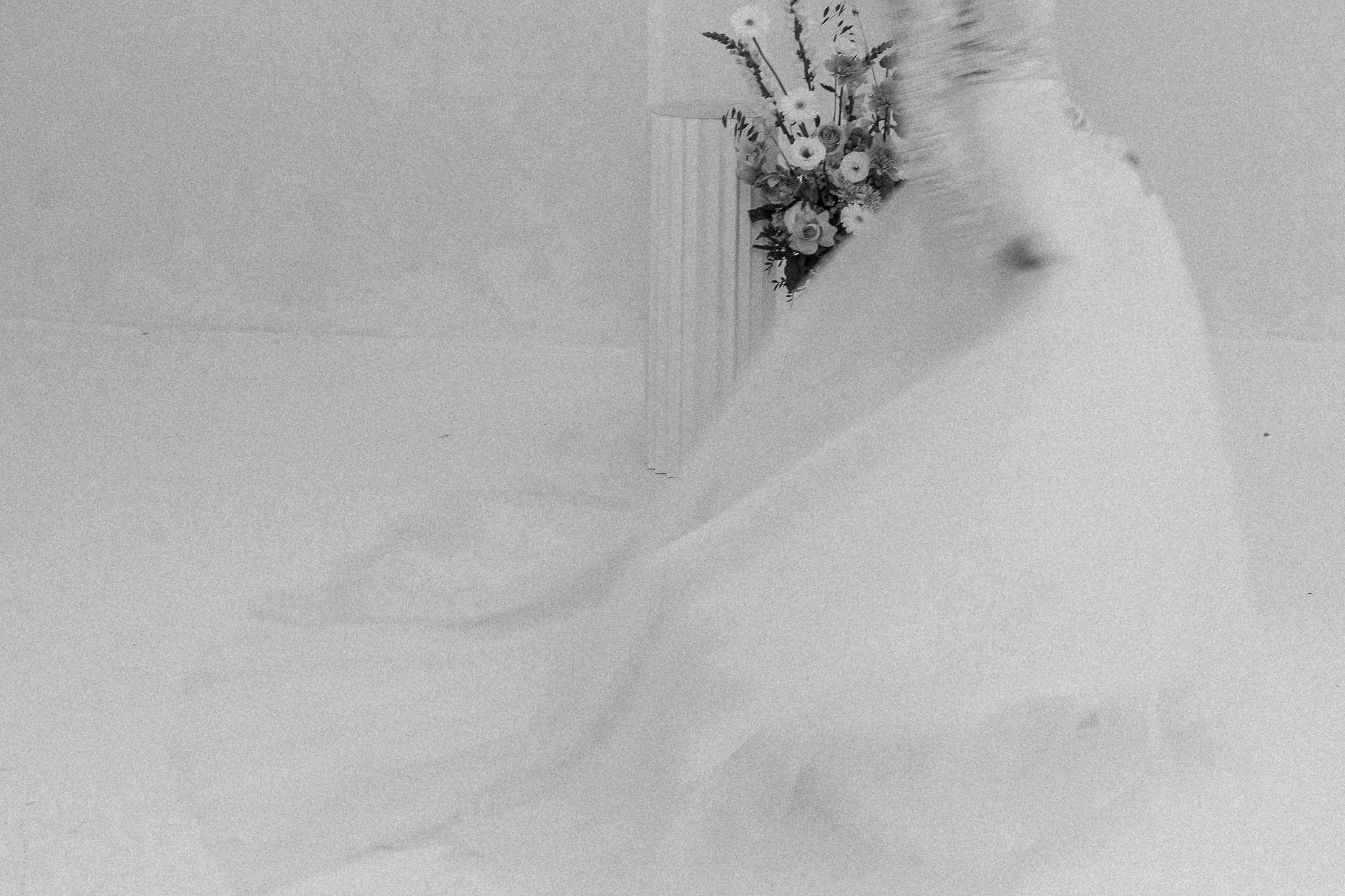 A bouquet of assorted flowers, including roses, in a tall, narrow vase on a table.