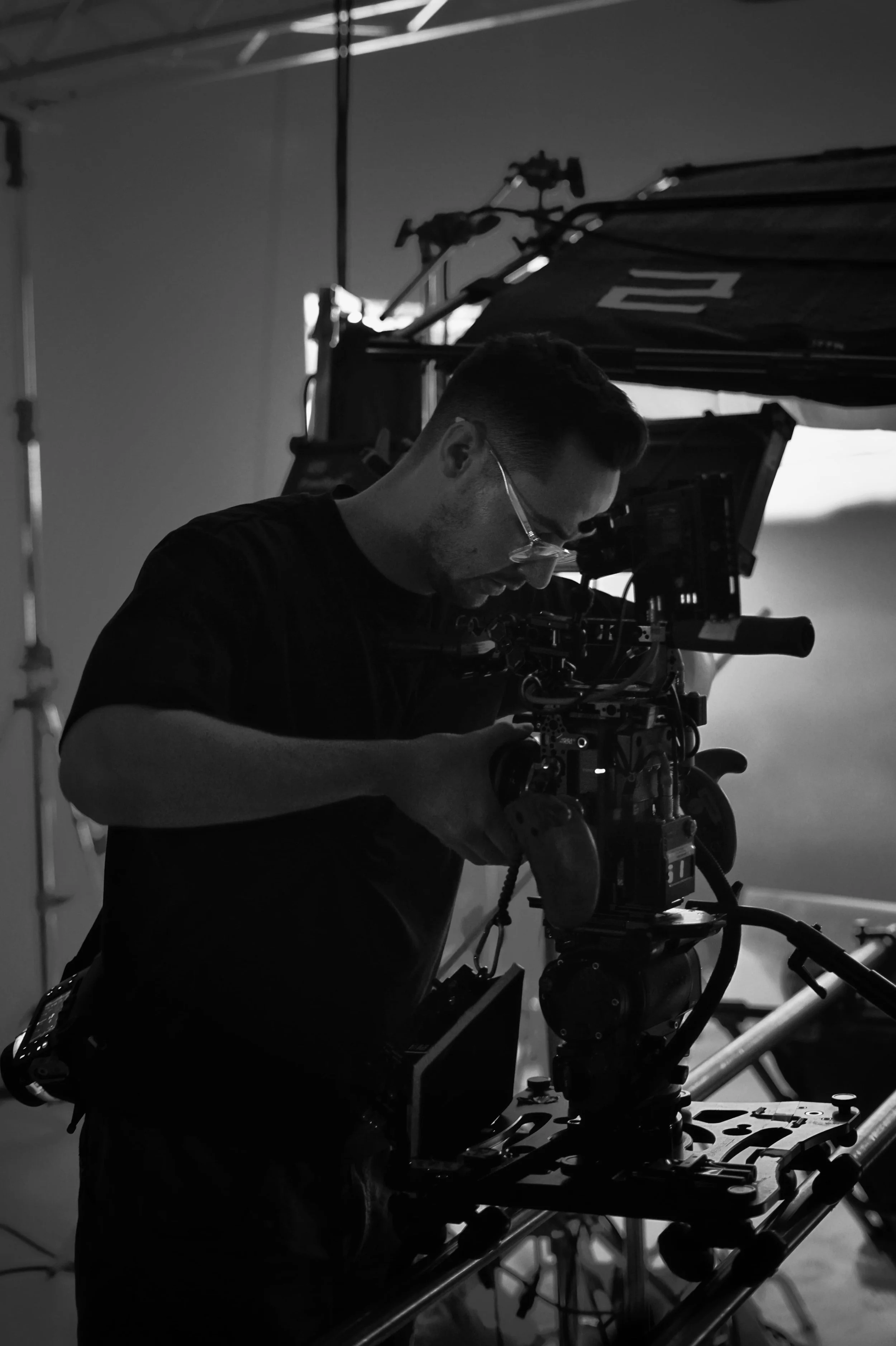 A man operating a professional camera on a film set, likely for filming or photography, in a dimly lit studio environment.