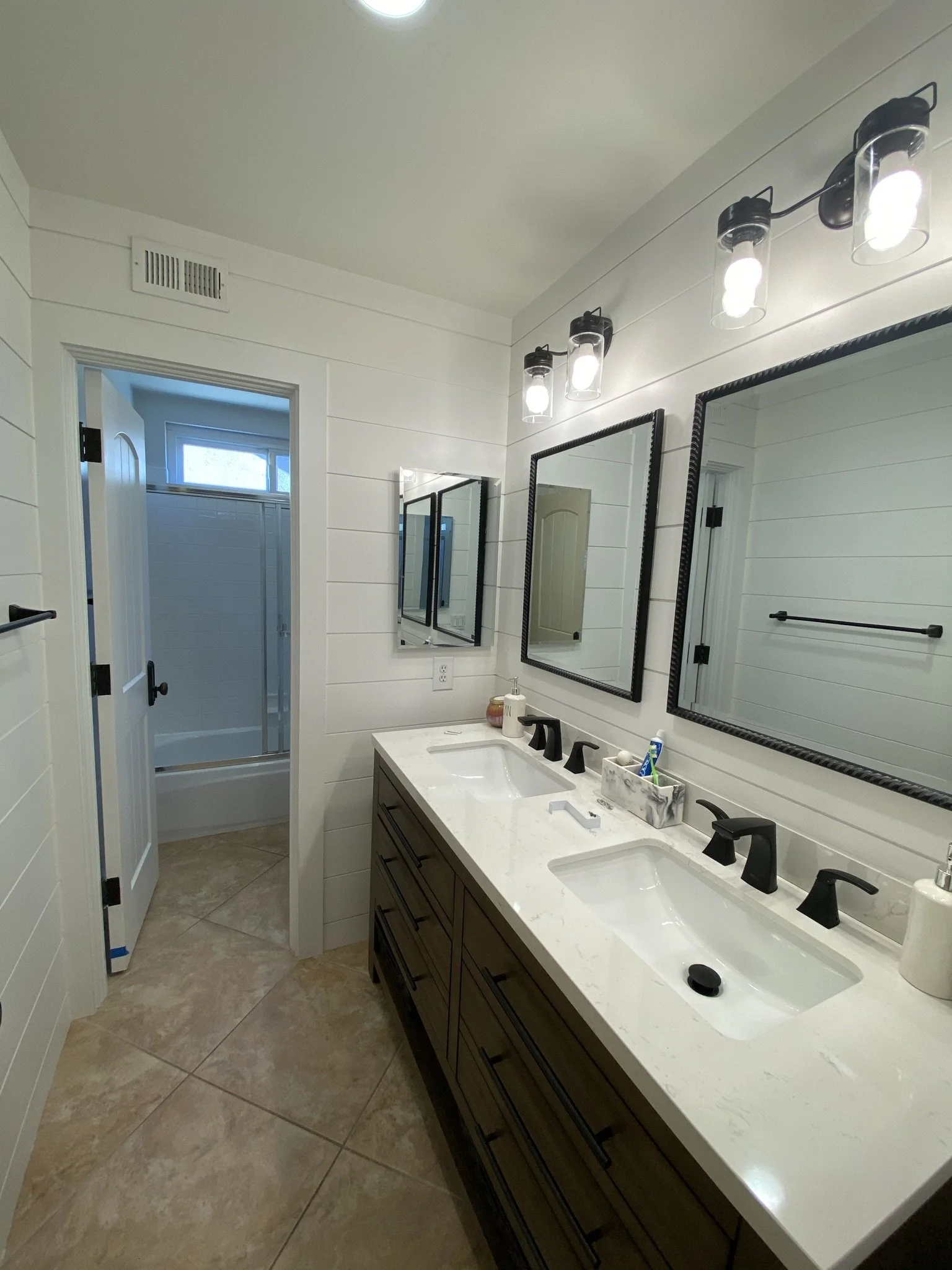 Designed with both style and utility in mind, this dual-sink bathroom features shiplap walls, oil-rubbed bronze hardware, and a quartz countertop with subtle veining.