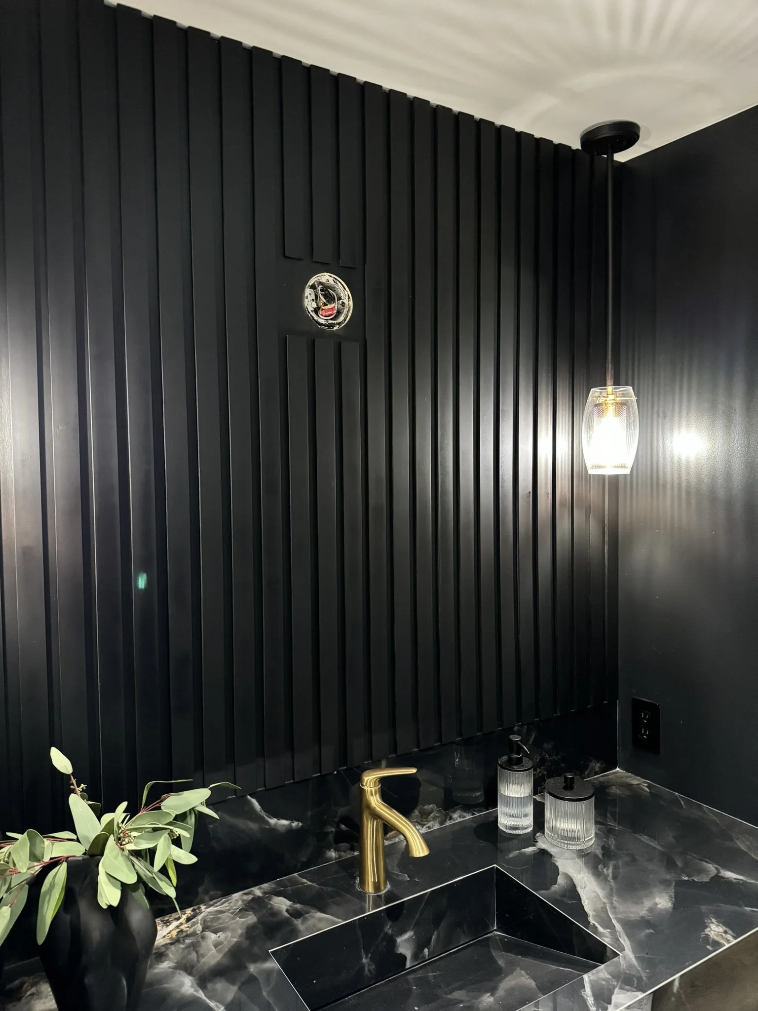 This bold powder room makes a striking first impression with matte black vertical paneling and a black marble waterfall countertop. Ideal for small spaces that want to make a big design statement.
