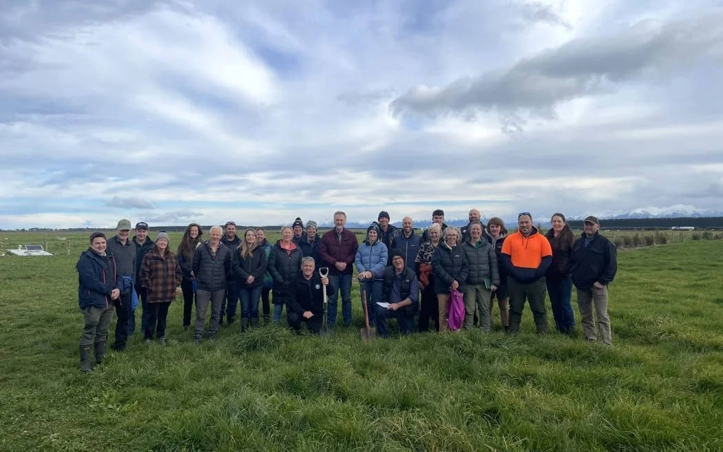 A group of 27 farmers standing in a field of diverse pasture