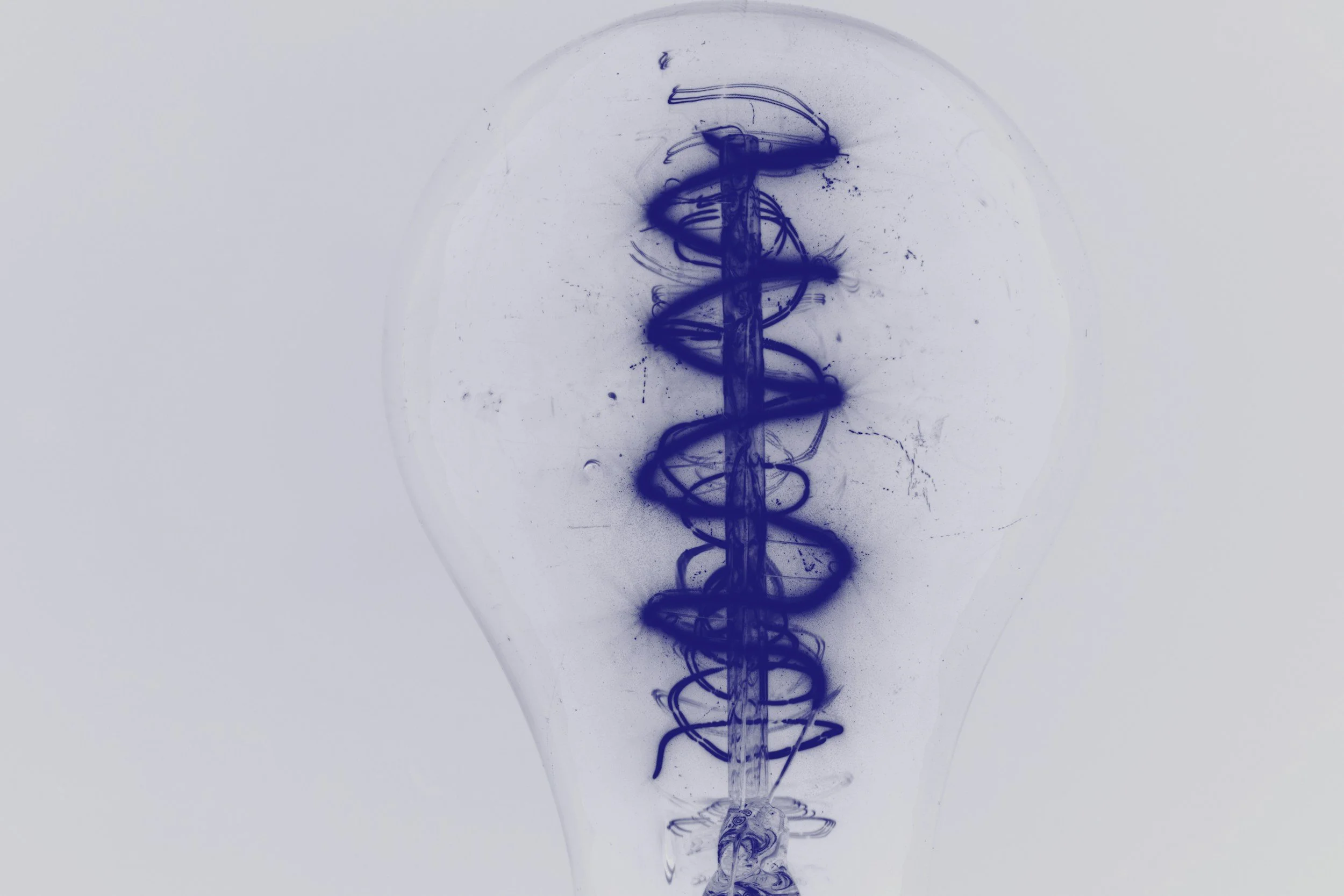 Una bombilla con una espiral de tinta azul formando un patrón en su interior.