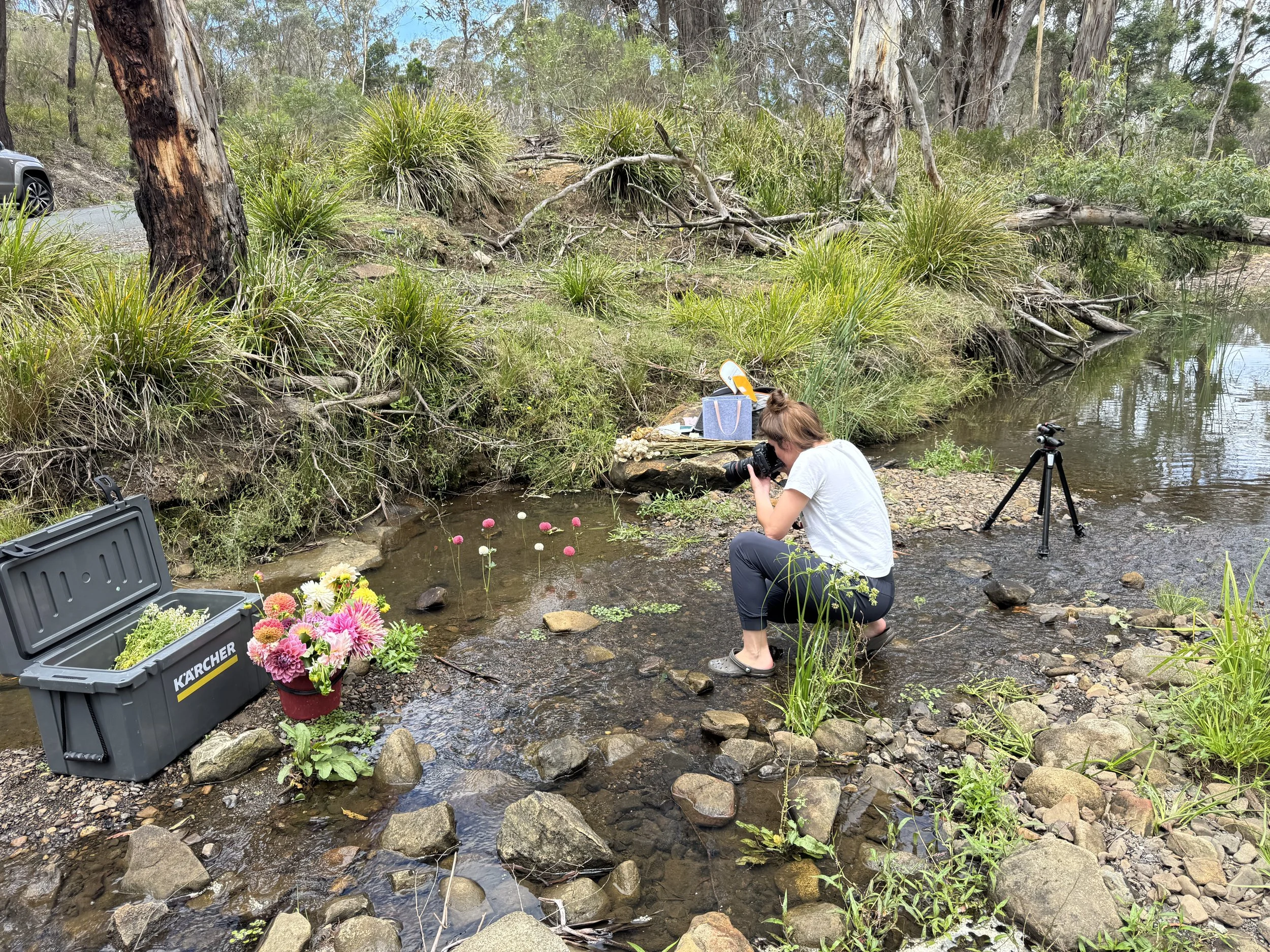 bébé bloom photographer Sarah Kinsella in action in our photoshoot set in a rocky creek bed with bunches of fresh flowers