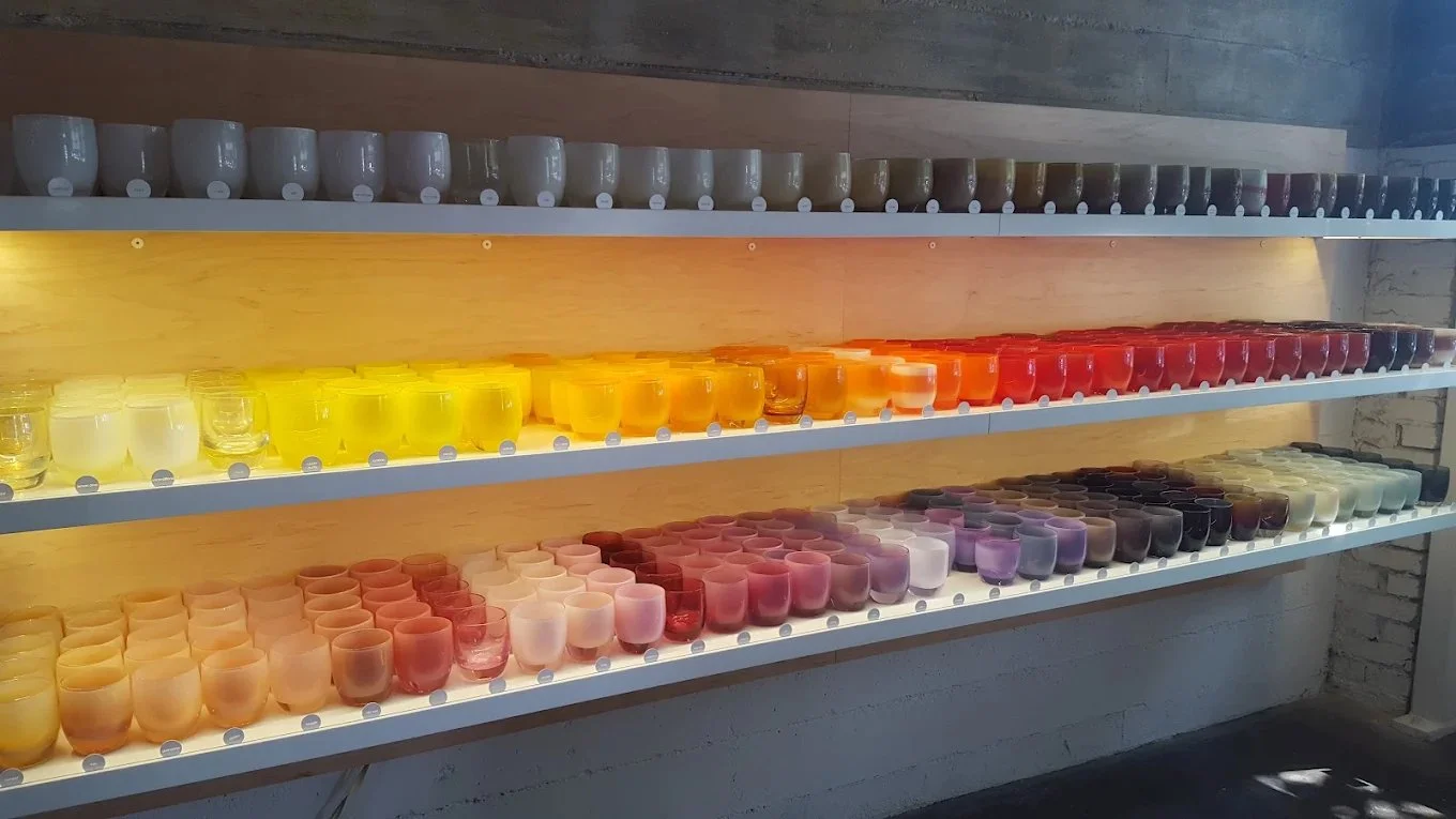 Colorful small candles or jars arranged on white shelves inside a room with a brick wall.