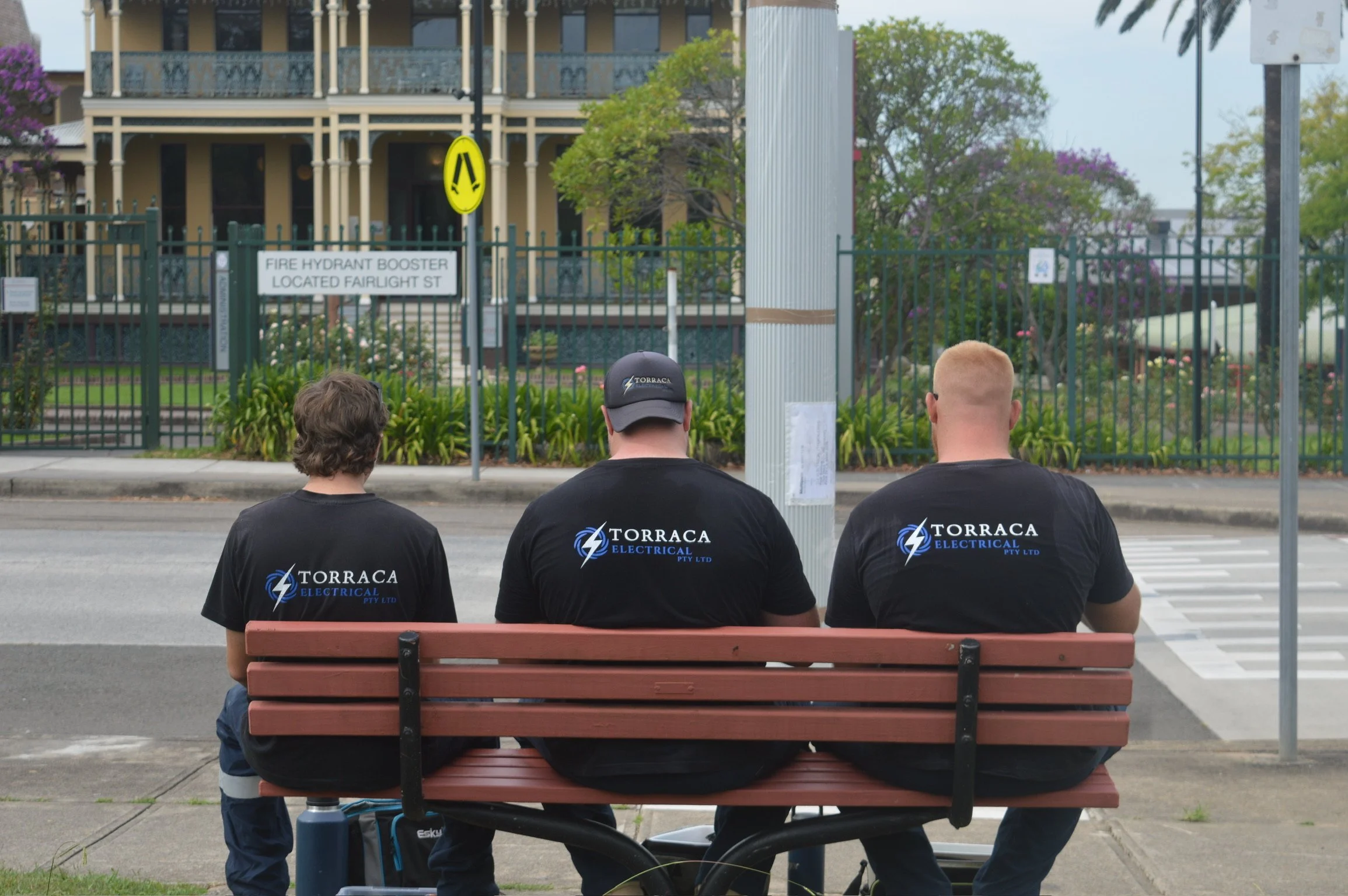 Three workers from Torraca Electrical sitting on a park bench, awaiting their next task.