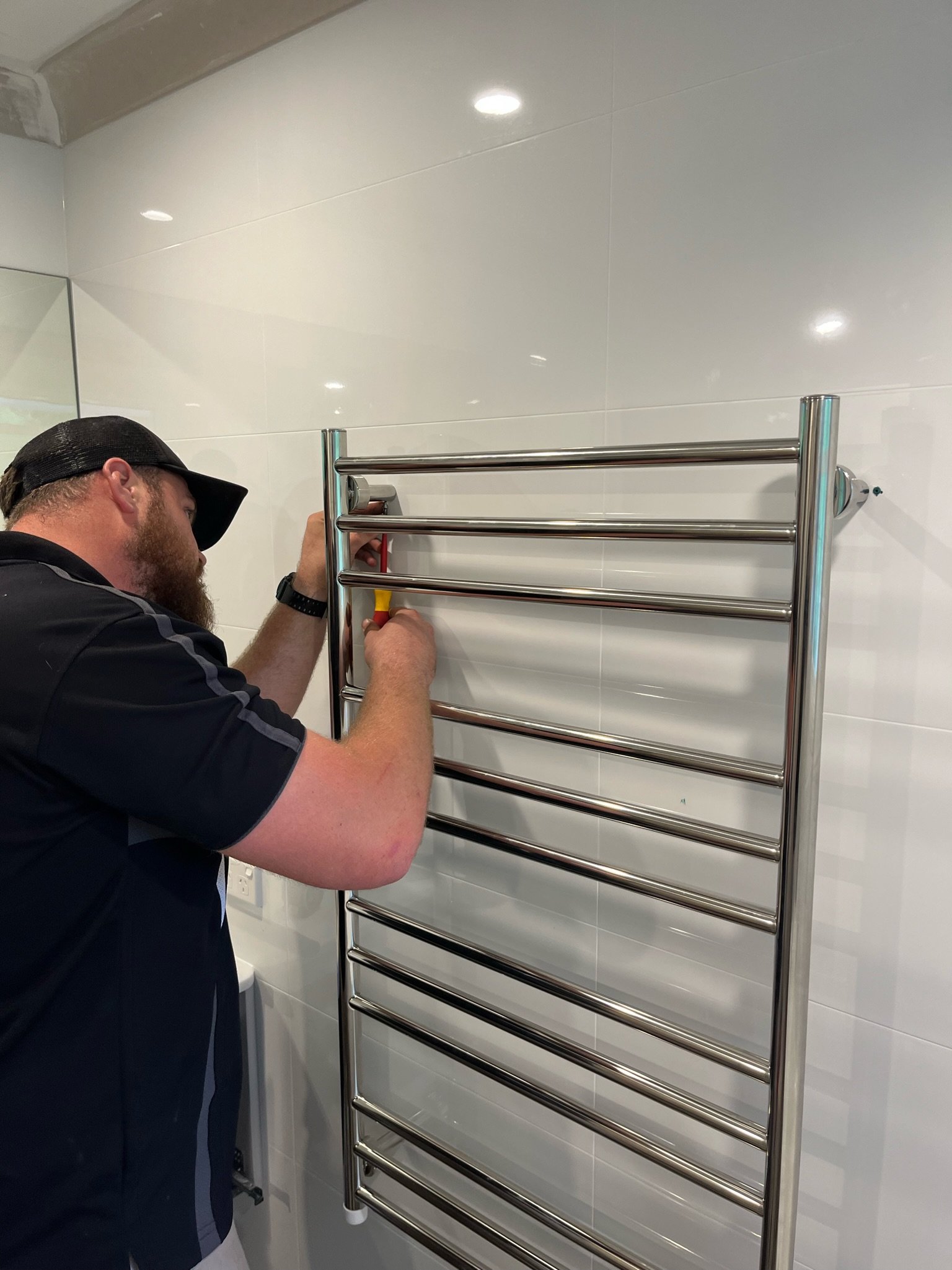 Man installing a towel warmer on a white tiled bathroom wall.