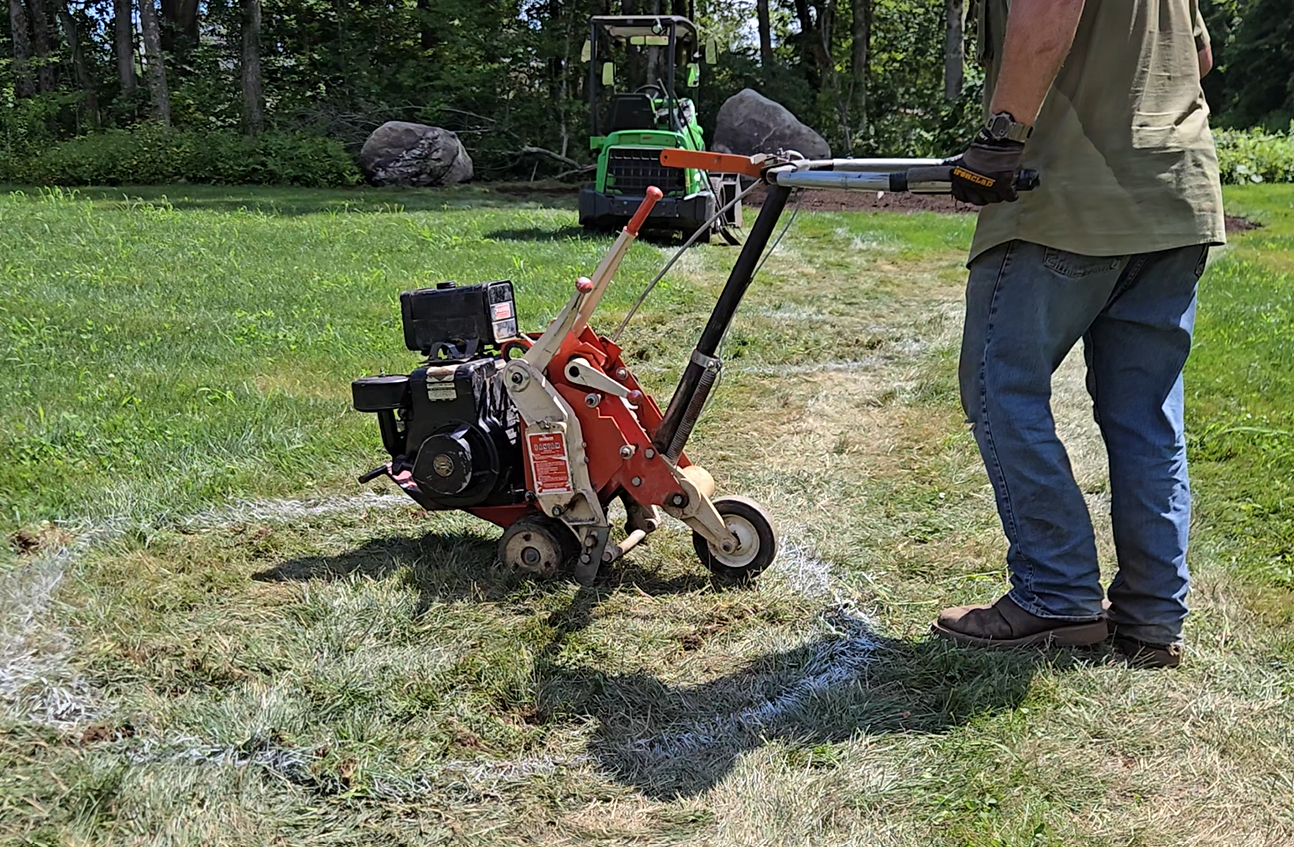 A professional garden installer operating a sod cutter on a grassy yard to install a beautiful garden by landscape design company Early Dawn Landscapes inc, in Danbury CT and surrounding CT and NY counties.