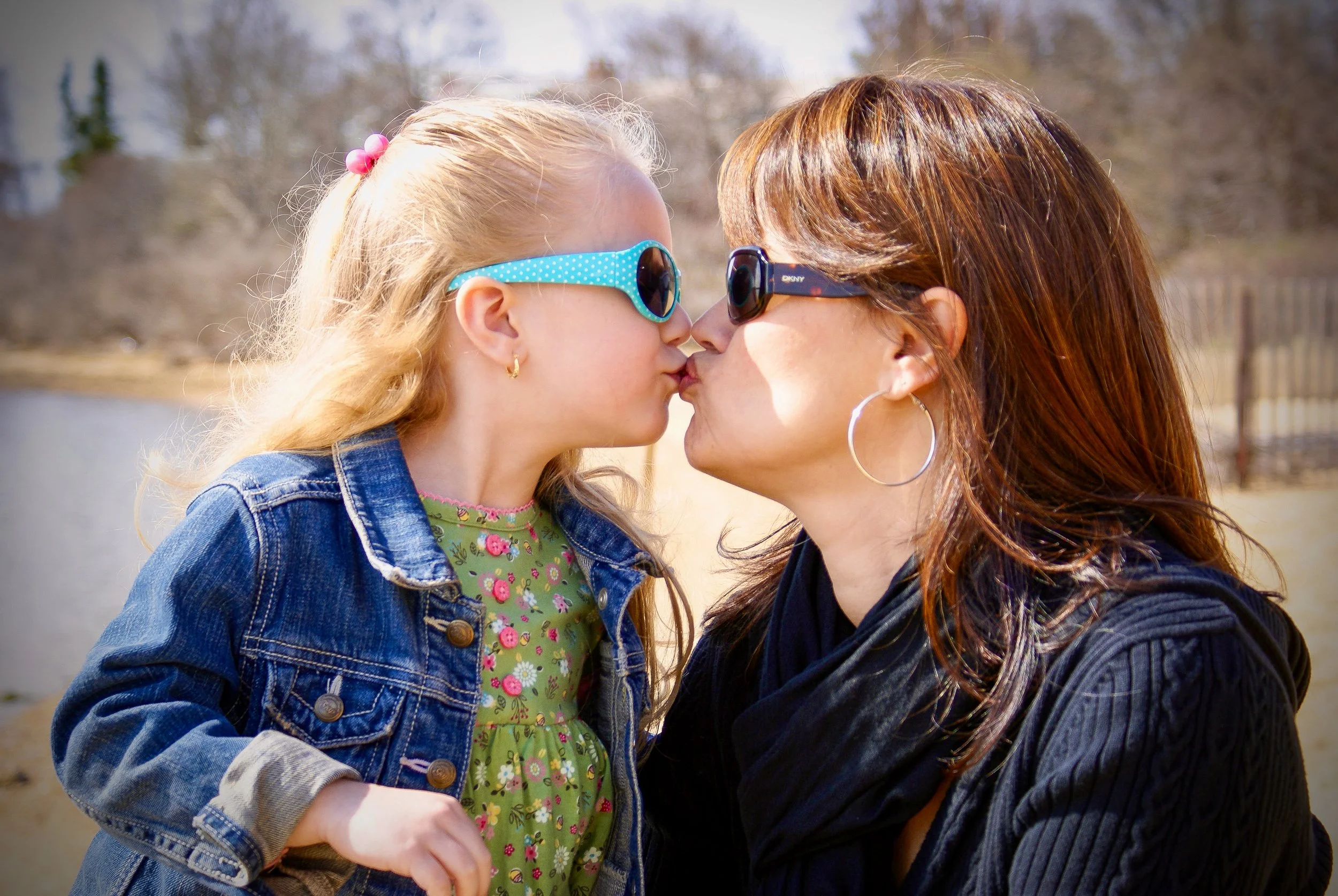 Candid moment of a mother and daughter sharing a kiss outdoors, unposed authentic family photography