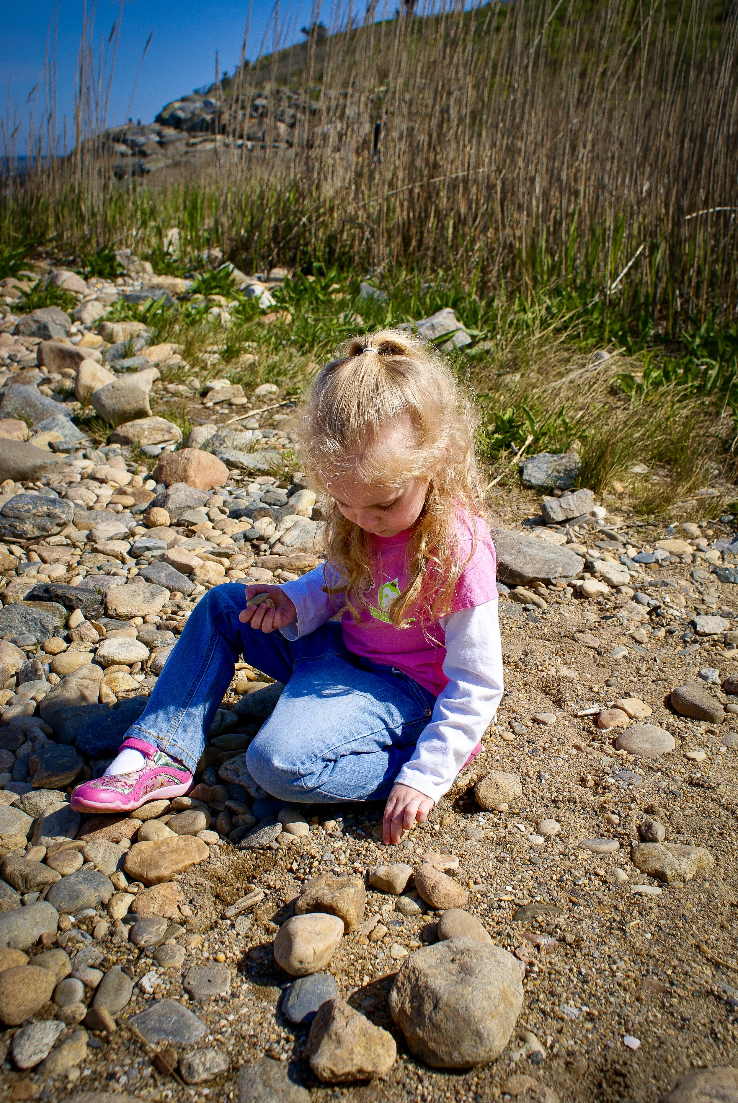 Young girl sitting on a rocky beach examining a stone, candid moment from an authentic NYC family photography session