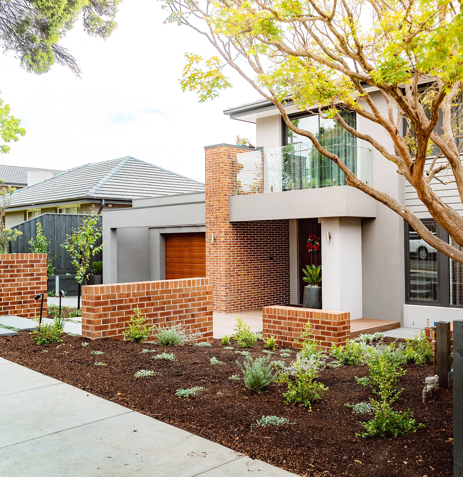 Modern house with a front yard, brick accents, brick and concrete walls, a small garden, and a large tree in the yard.