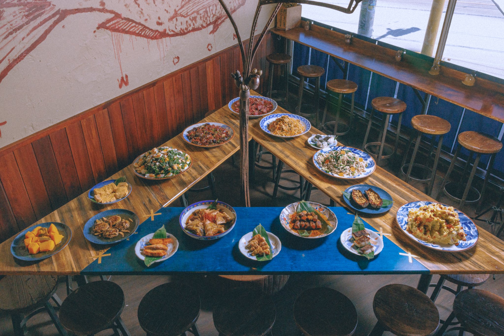 Wooden tables with an assortment of Asian dishes, plates, and bowls in a rustic restaurant setting with wooden stools.