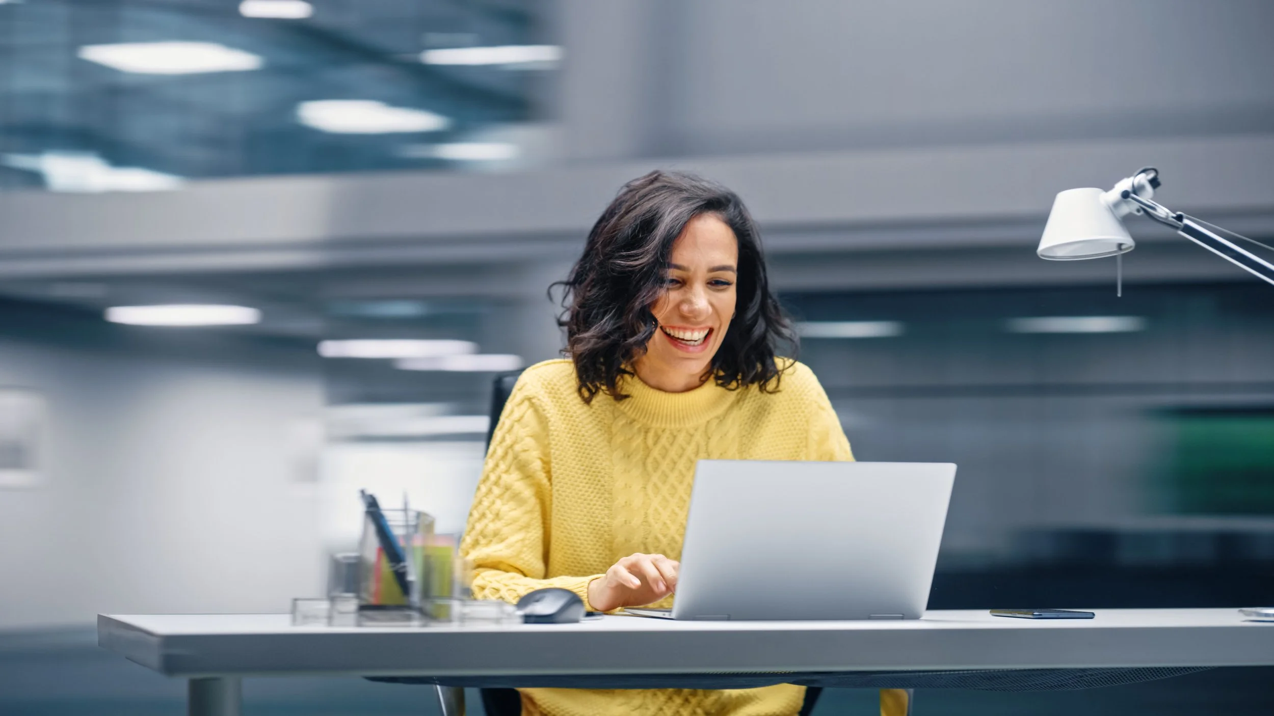 Mujer sonriendo mientras trabaja en una computadora portátil en una oficina moderna.