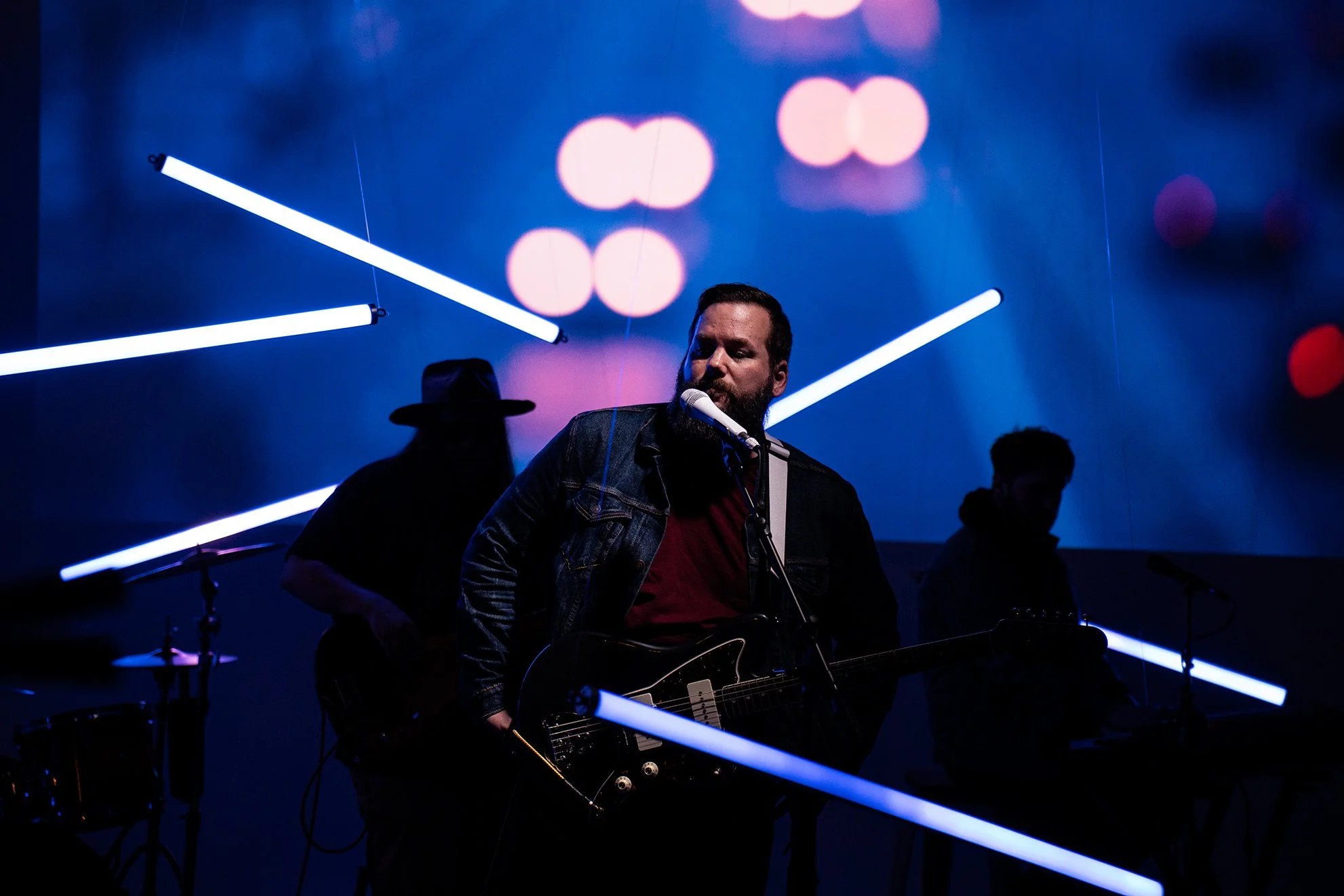 Musician with moody lighting and bandmates in show behind him. Projector image on wall behind.