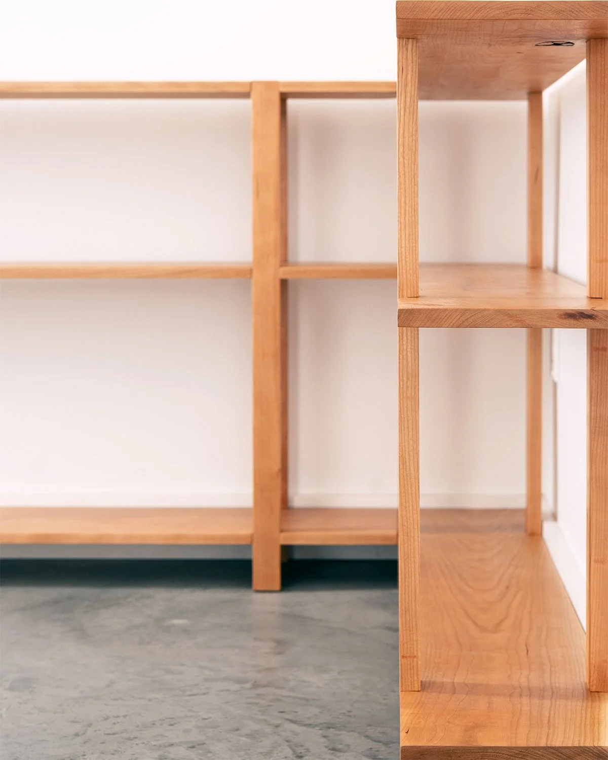 A pair of solid black cherry wood bookshelves, arranged in their corner configuration, handmade in Nelson BC Canada.
