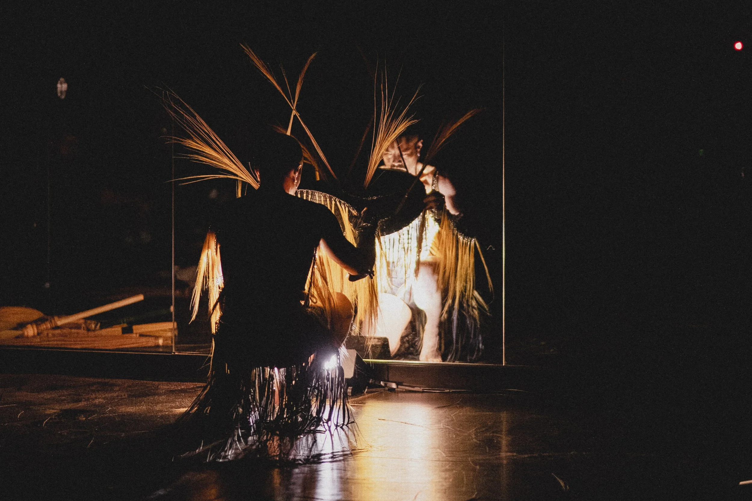 A performer is silhoutted against a bright background during a fire dance, holding flaming props with sparks flying in the dark.