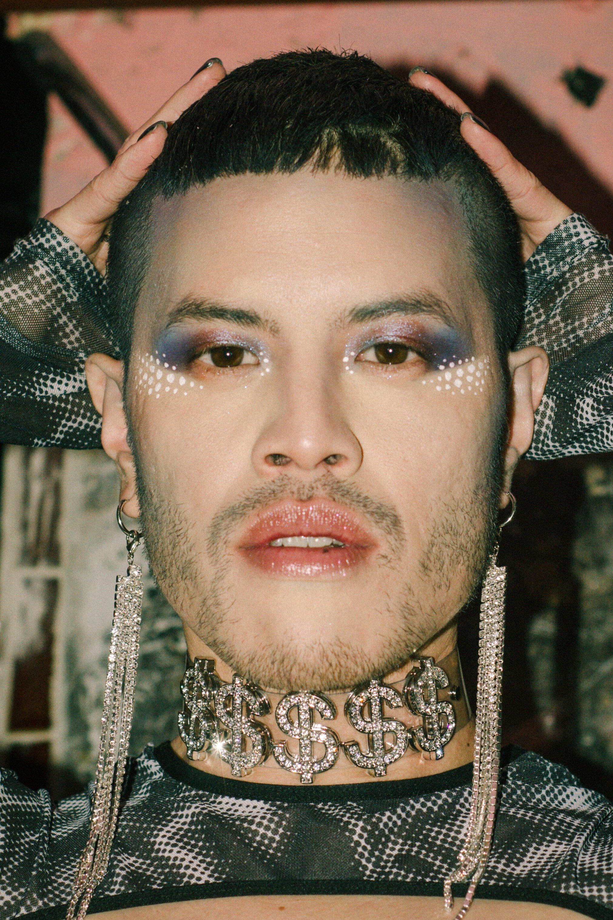 Close-up of a person with colorful eye makeup, dotted face decorations, glittery earrings, and a dollar sign choker necklace.