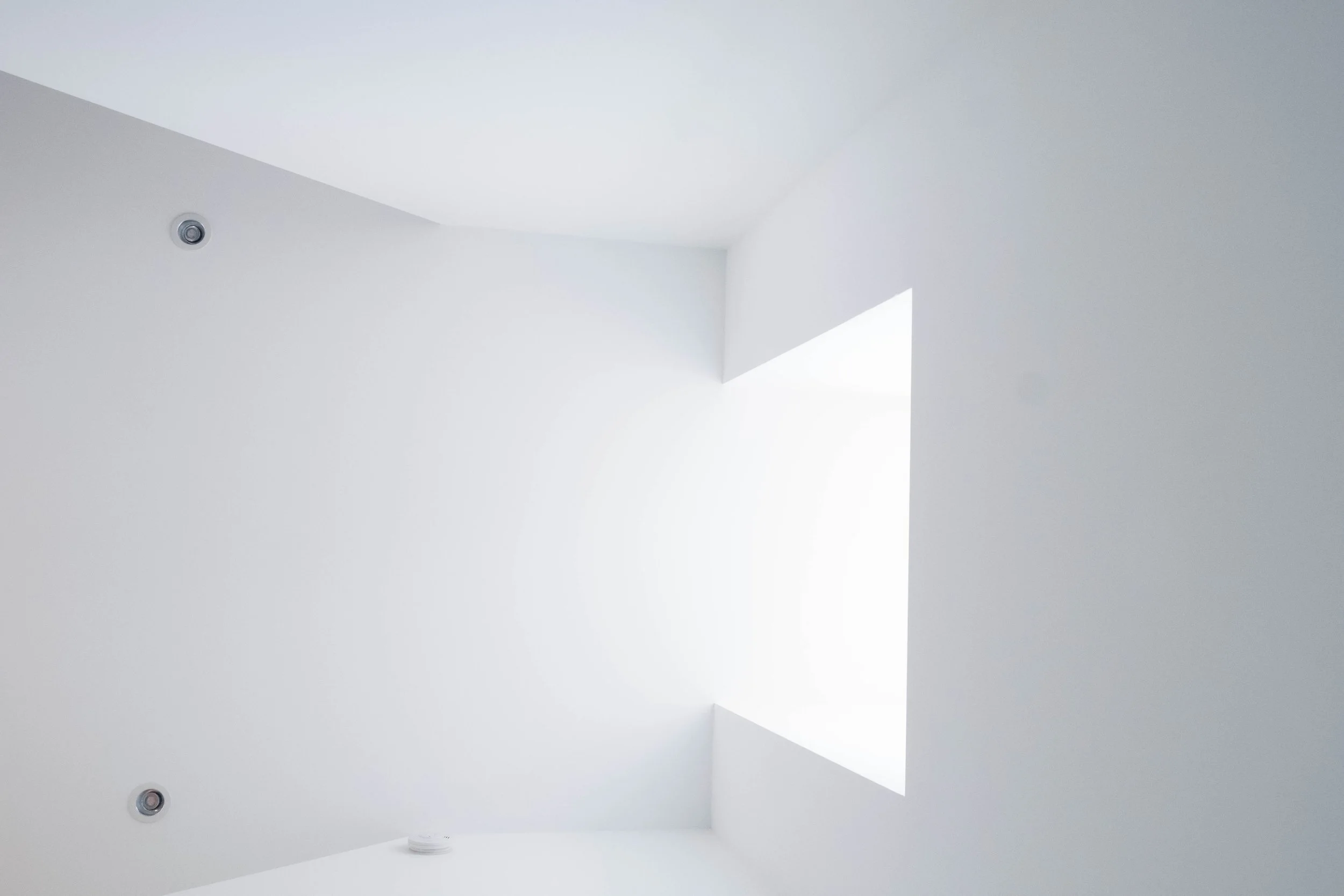 A minimalist white ceiling with recessed lights and a large rectangular skylight.