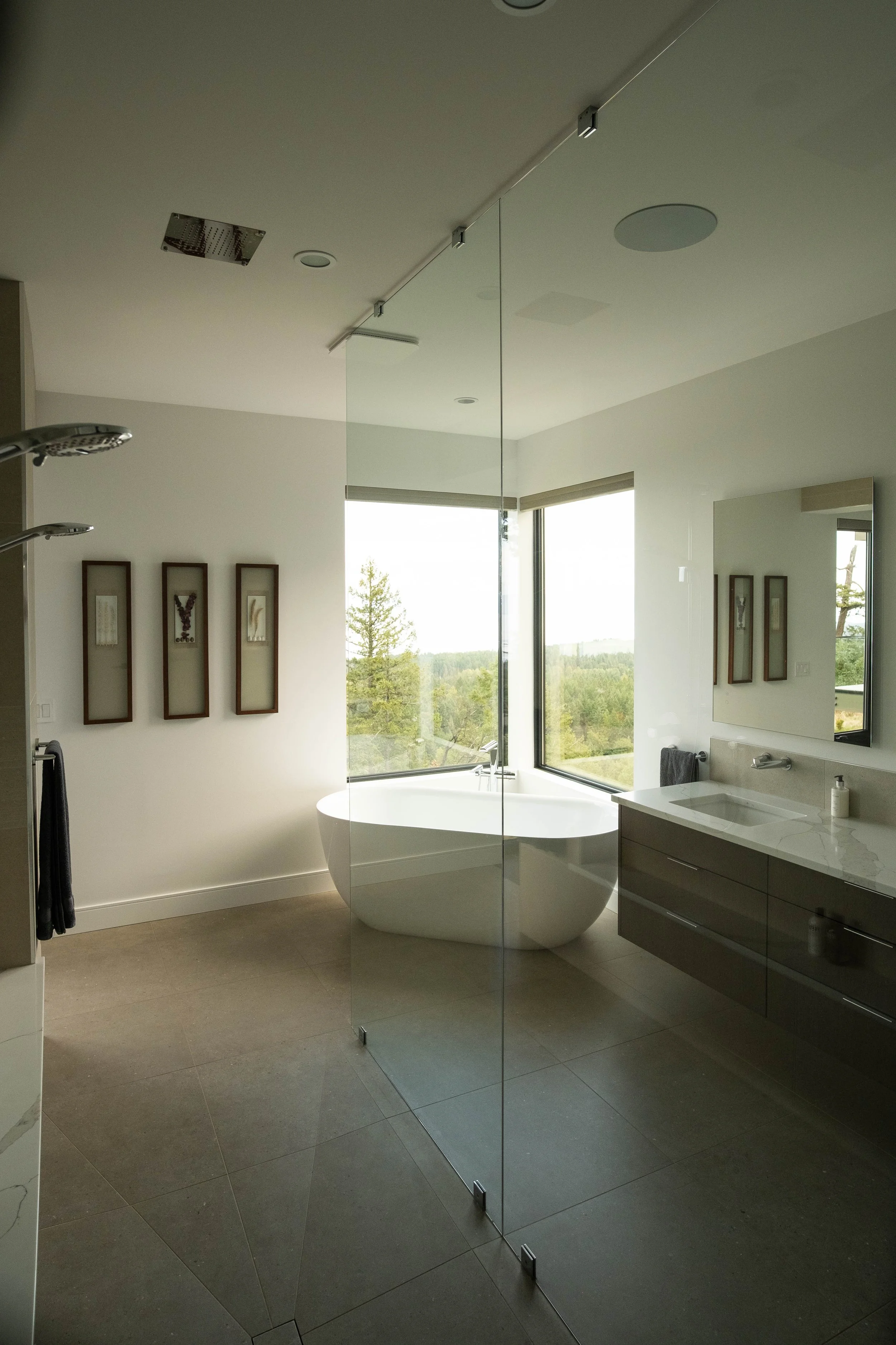 Modern bathroom with a freestanding bathtub near large windows showing a scenic outdoor view, a floating vanity with a sink, a mirror, and minimalist decor.