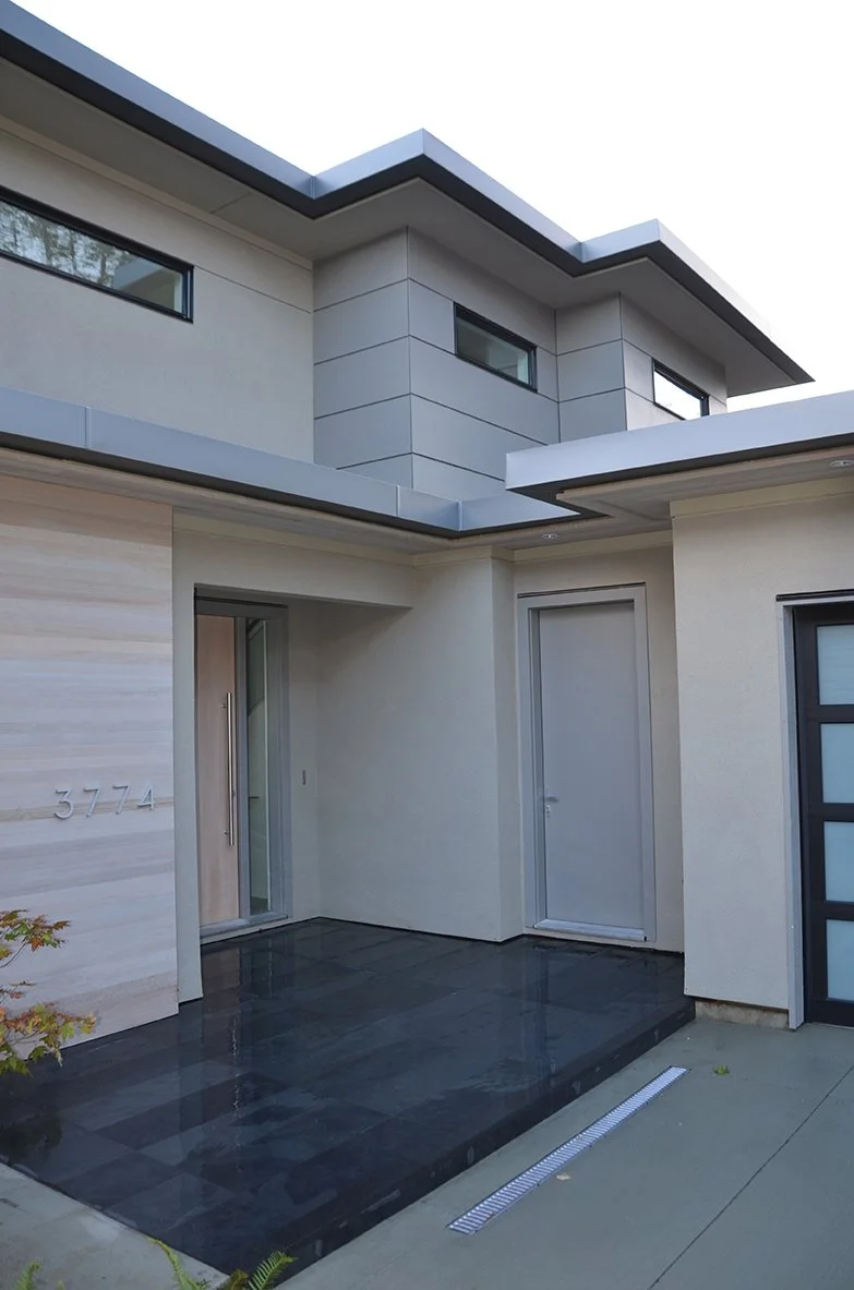 Modern house exterior with a small covered entryway, black tiled porch, and gray exterior walls with horizontal lines.