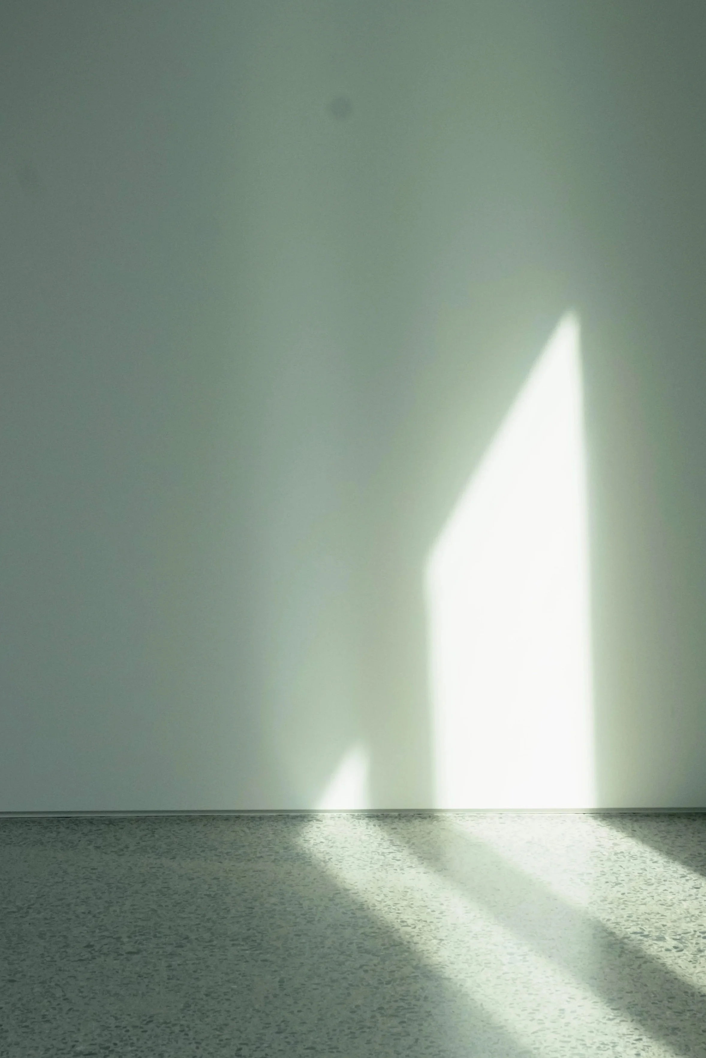 Sunlight creating geometric shadow patterns on a white wall and speckled gray floor.