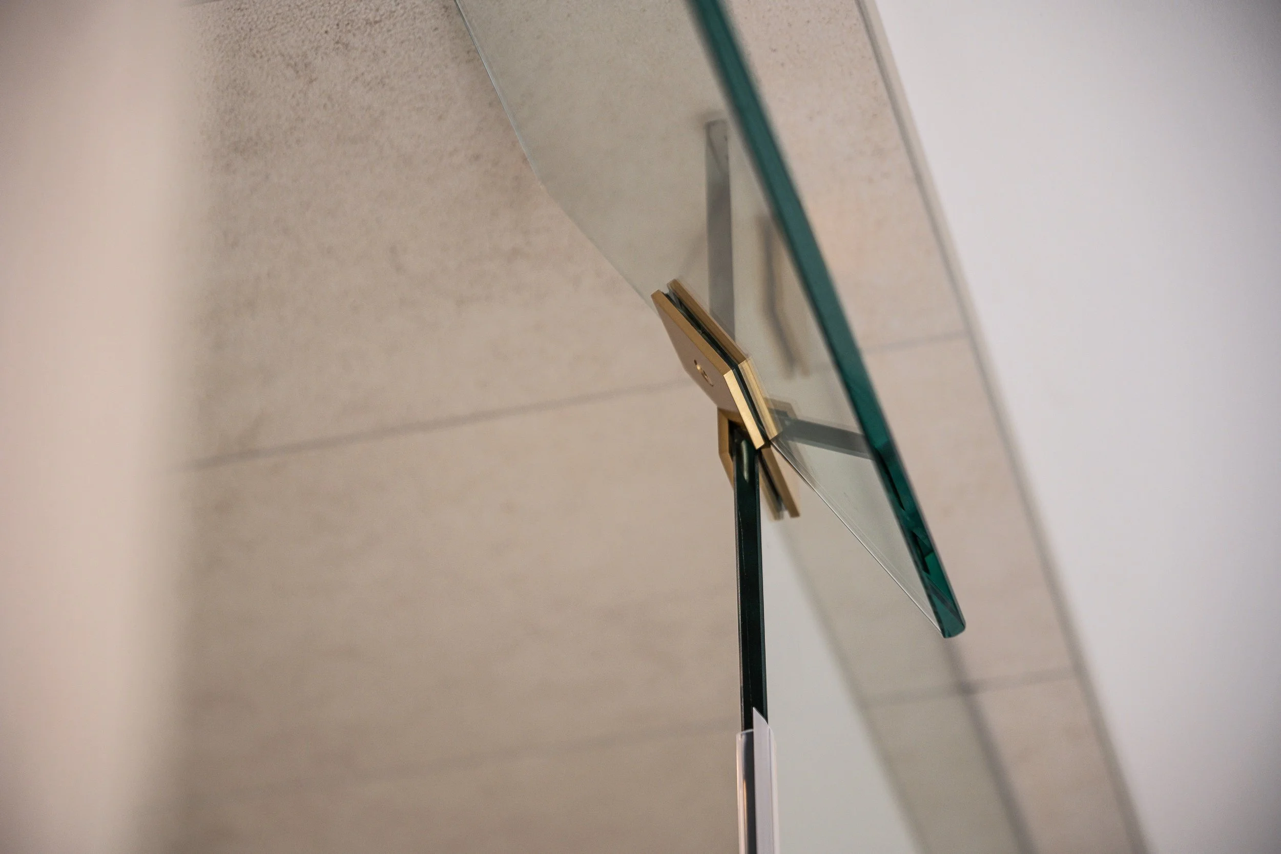 Close-up of a modern glass wall clock with black and gold hands, mounted on a concrete wall.