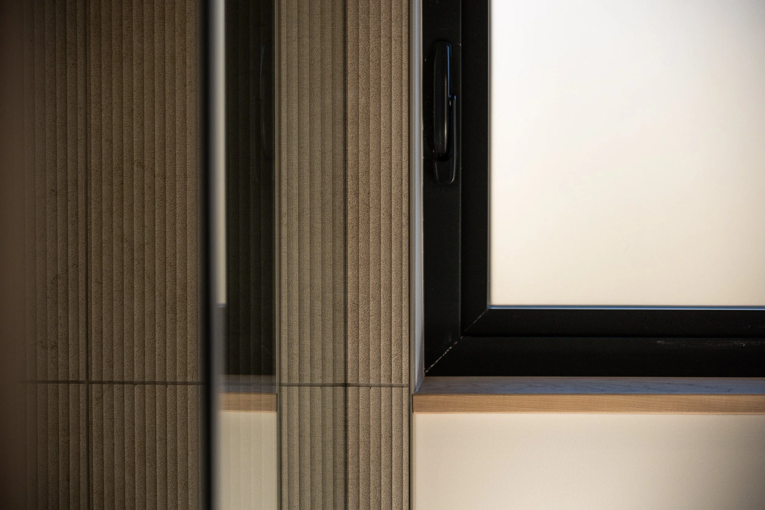 Close-up of a corner of a modern window with a black frame, brown textured wall, and beige wall underneath.