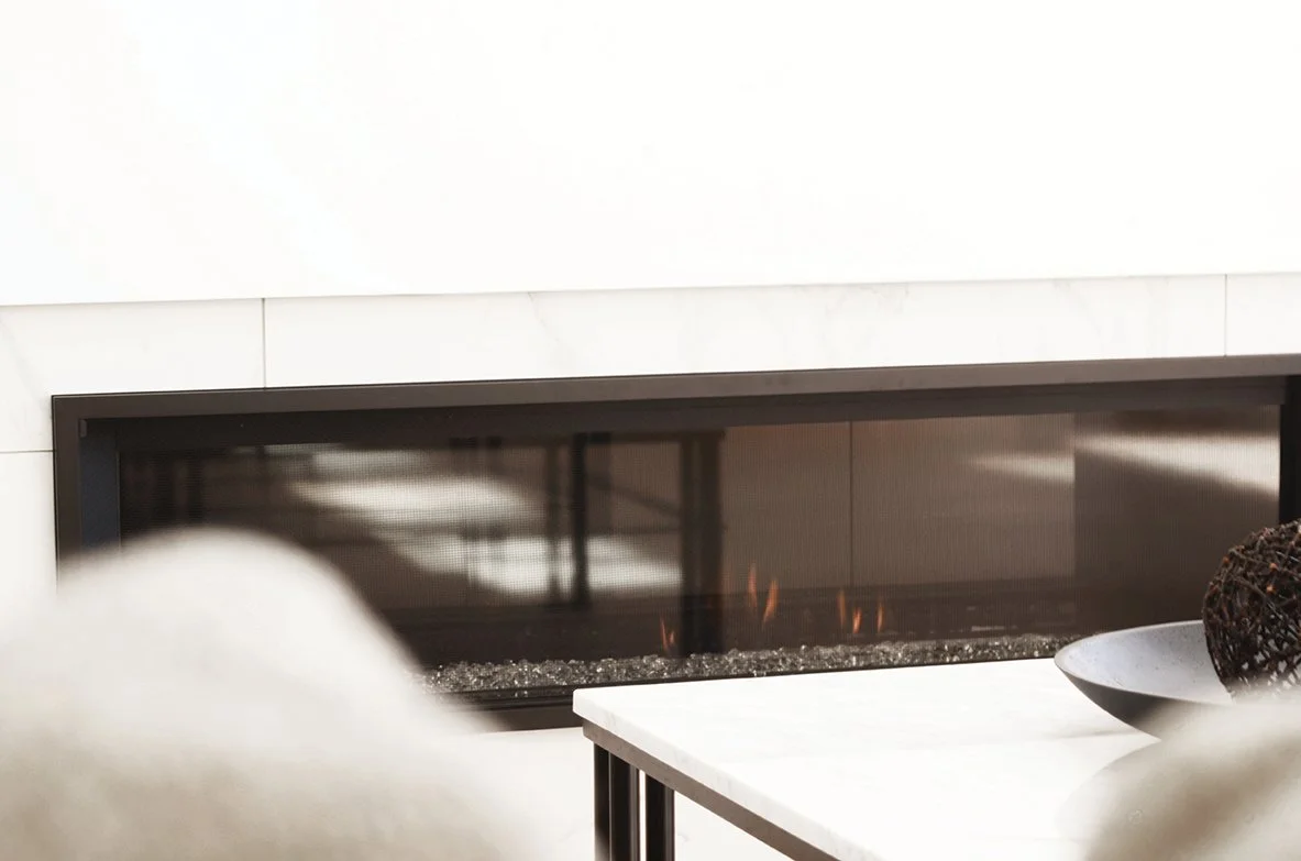 Modern fireplace with a glass front and visible flames, adjacent to a white marble tabletop with decorative bowls.