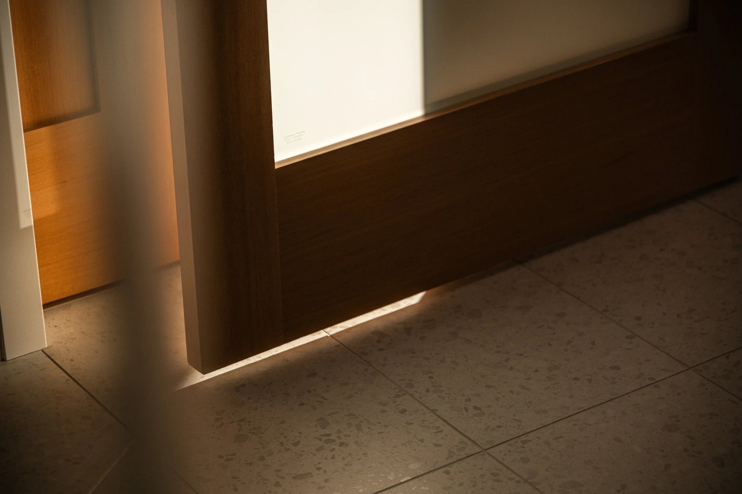 Close-up of a wooden door with a gap at the bottom, with light shining through the gap onto the tiled floor.