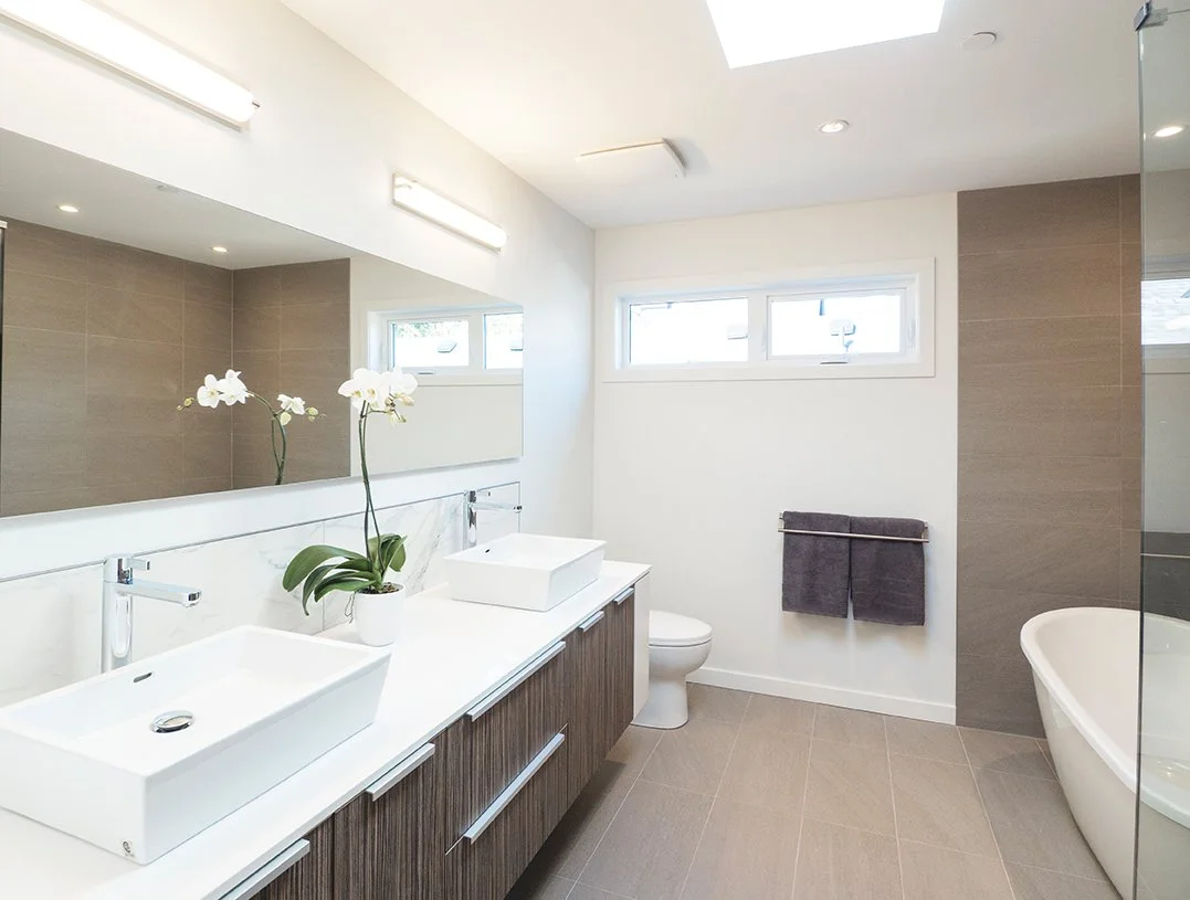 Modern bathroom with double vanity, rectangular vessel sinks, large mirror, orchid plant, toilet, bathtub, and small horizontal windows.