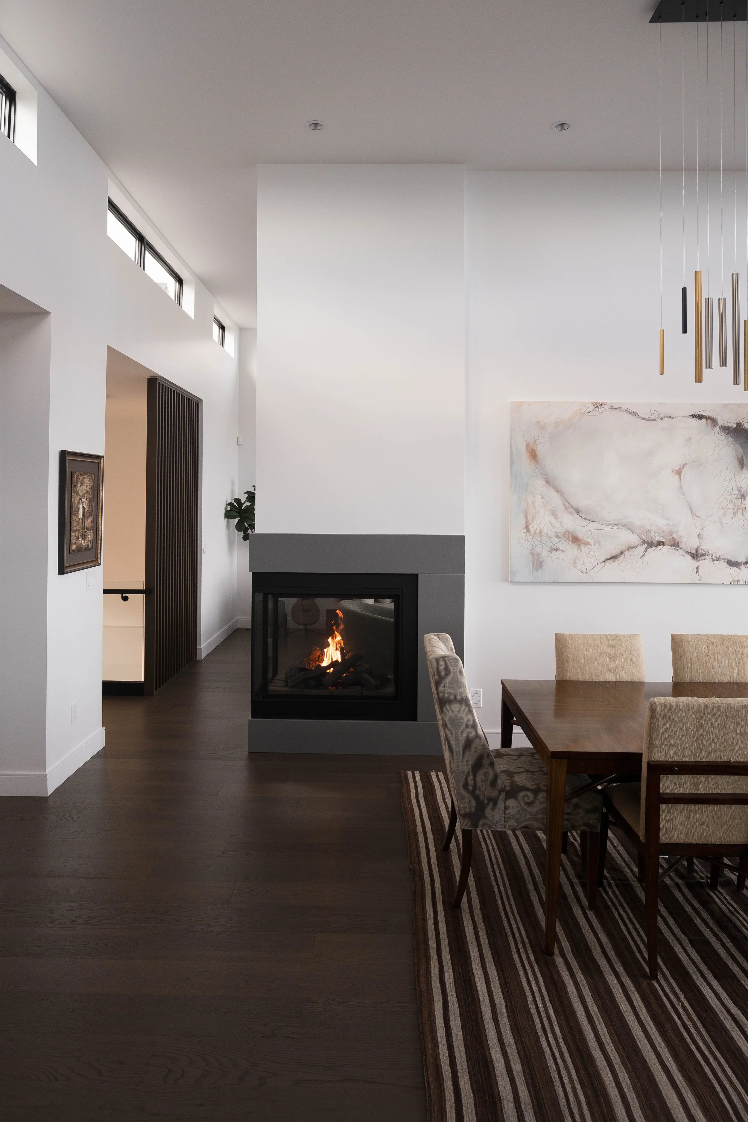 Modern living room with a fireplace, dining table, and artwork on white walls.