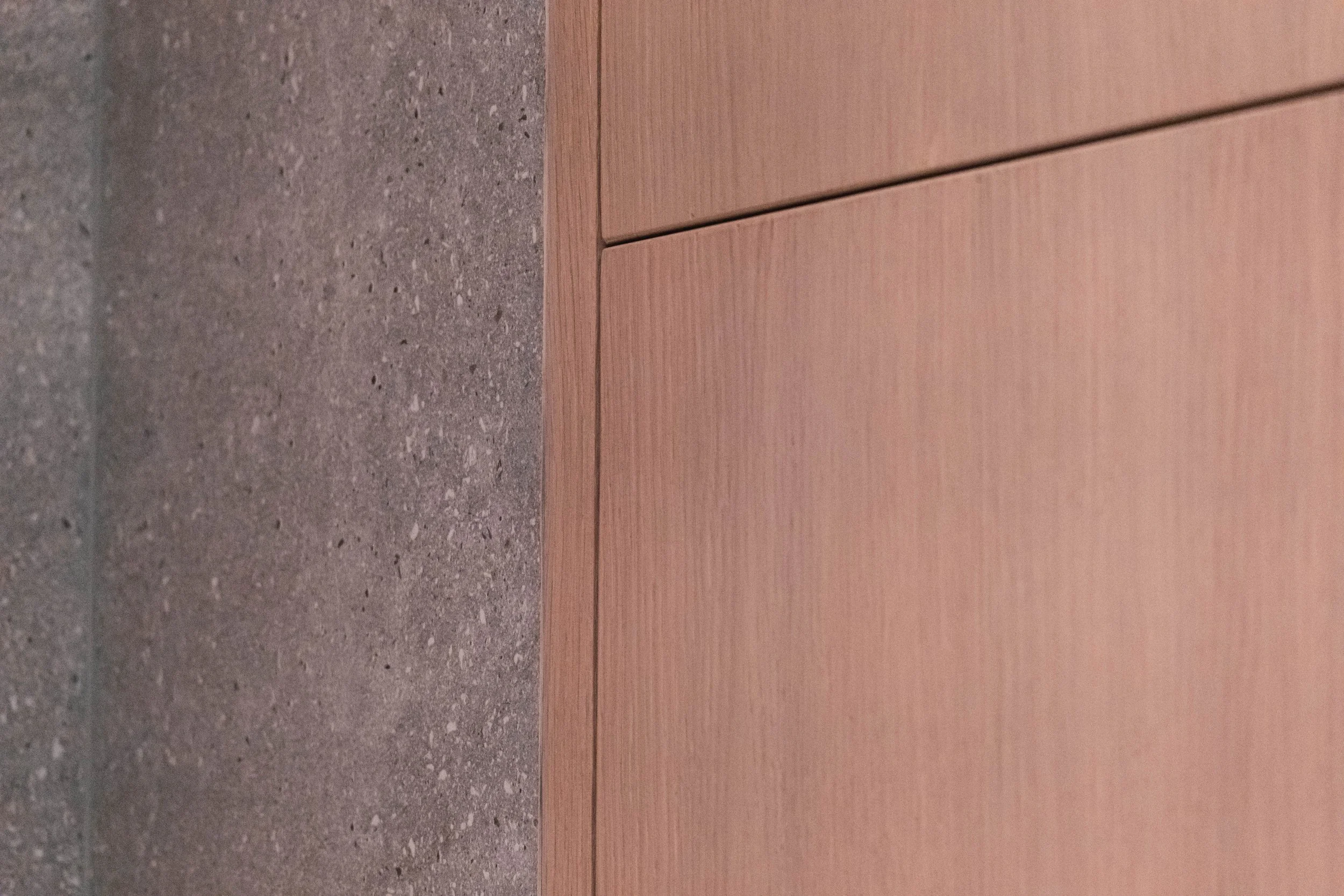 Close-up of a corner where a concrete wall meets a light wood-finished panel.