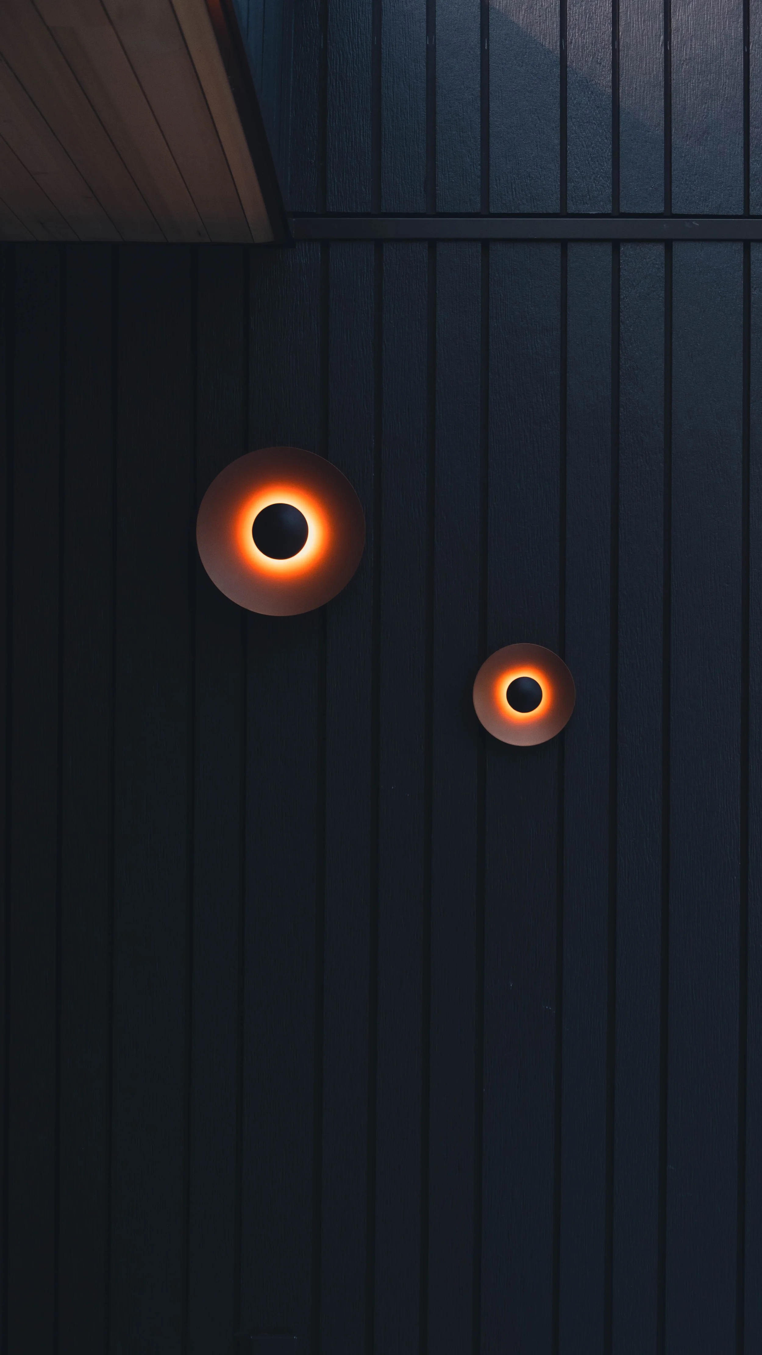 Two circular ceiling lights with warm orange glow on a dark, wood-paneled ceiling.