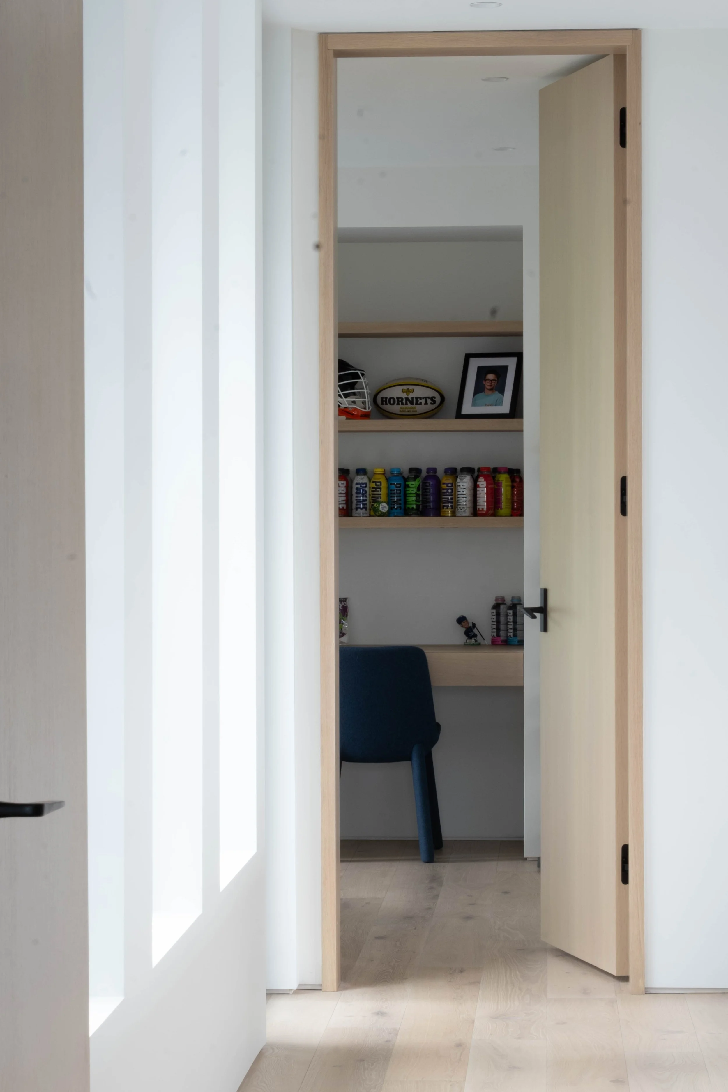View through a doorway into a small room with a desk, a blue chair, and shelves holding sports memorabilia and colorful cans.