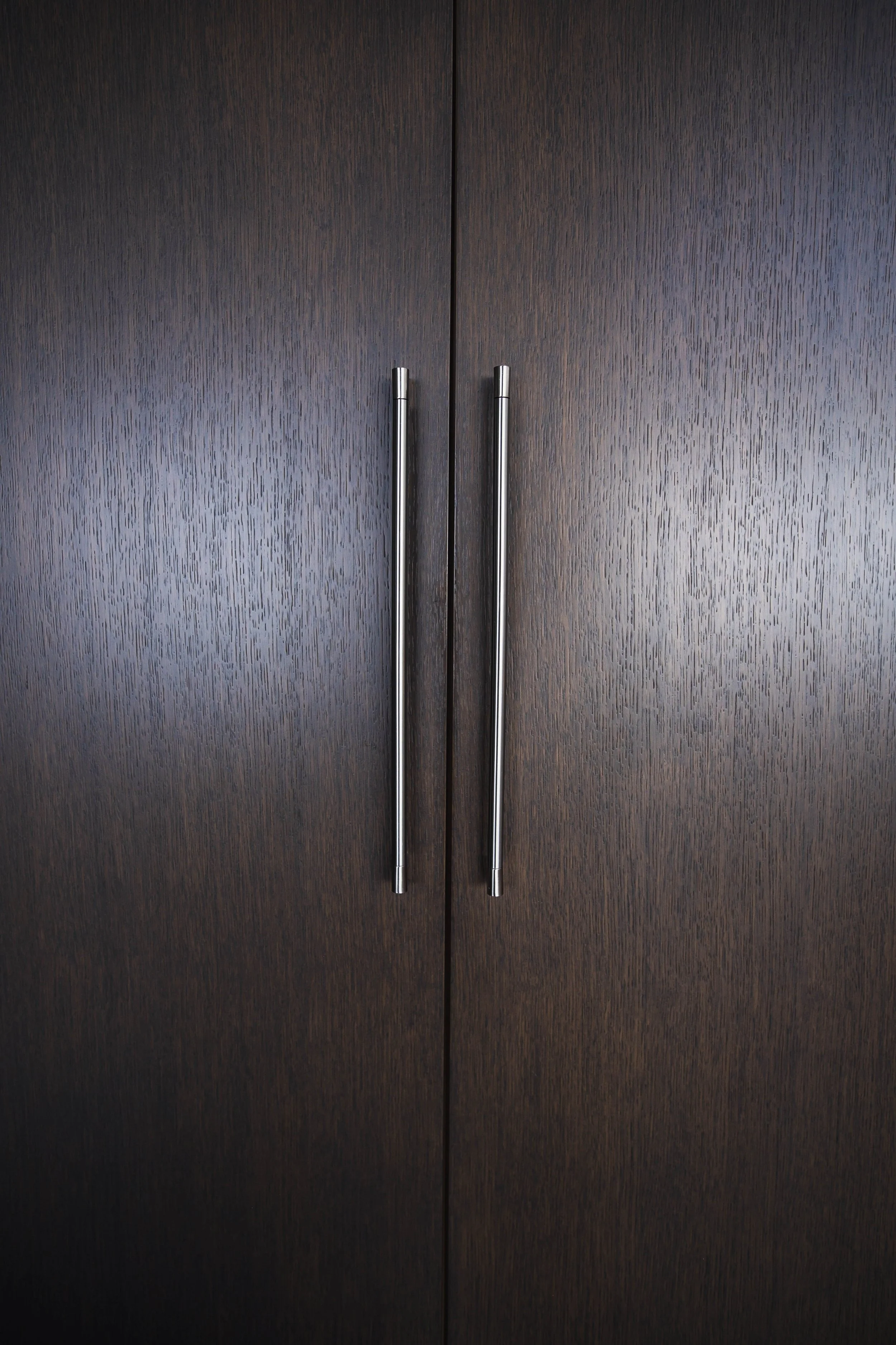 Close-up of dark wood cabinet doors with two silver vertical handles.