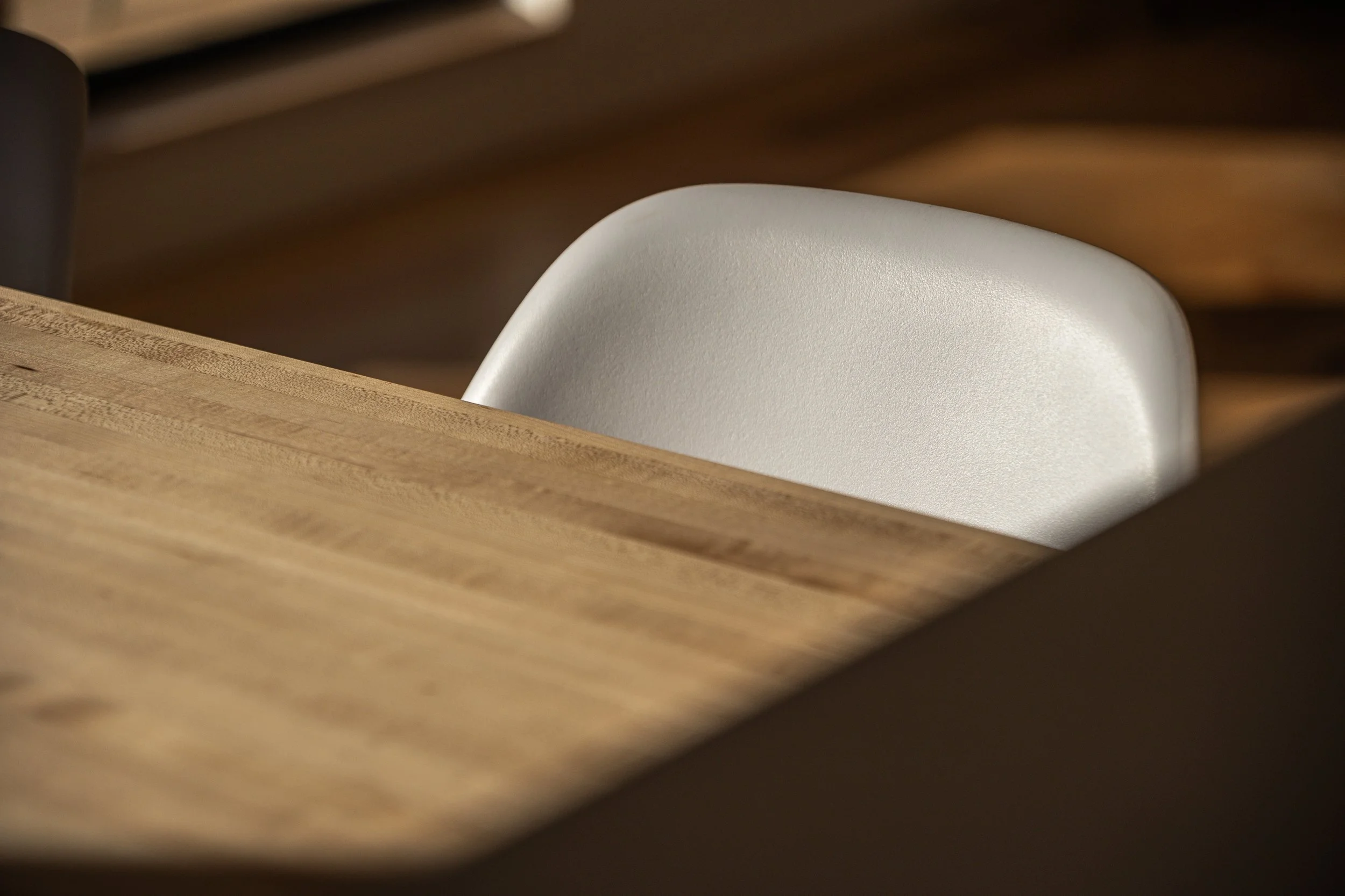 Close-up of a white chair partially hidden behind a wooden table or counter, with a blurred background.