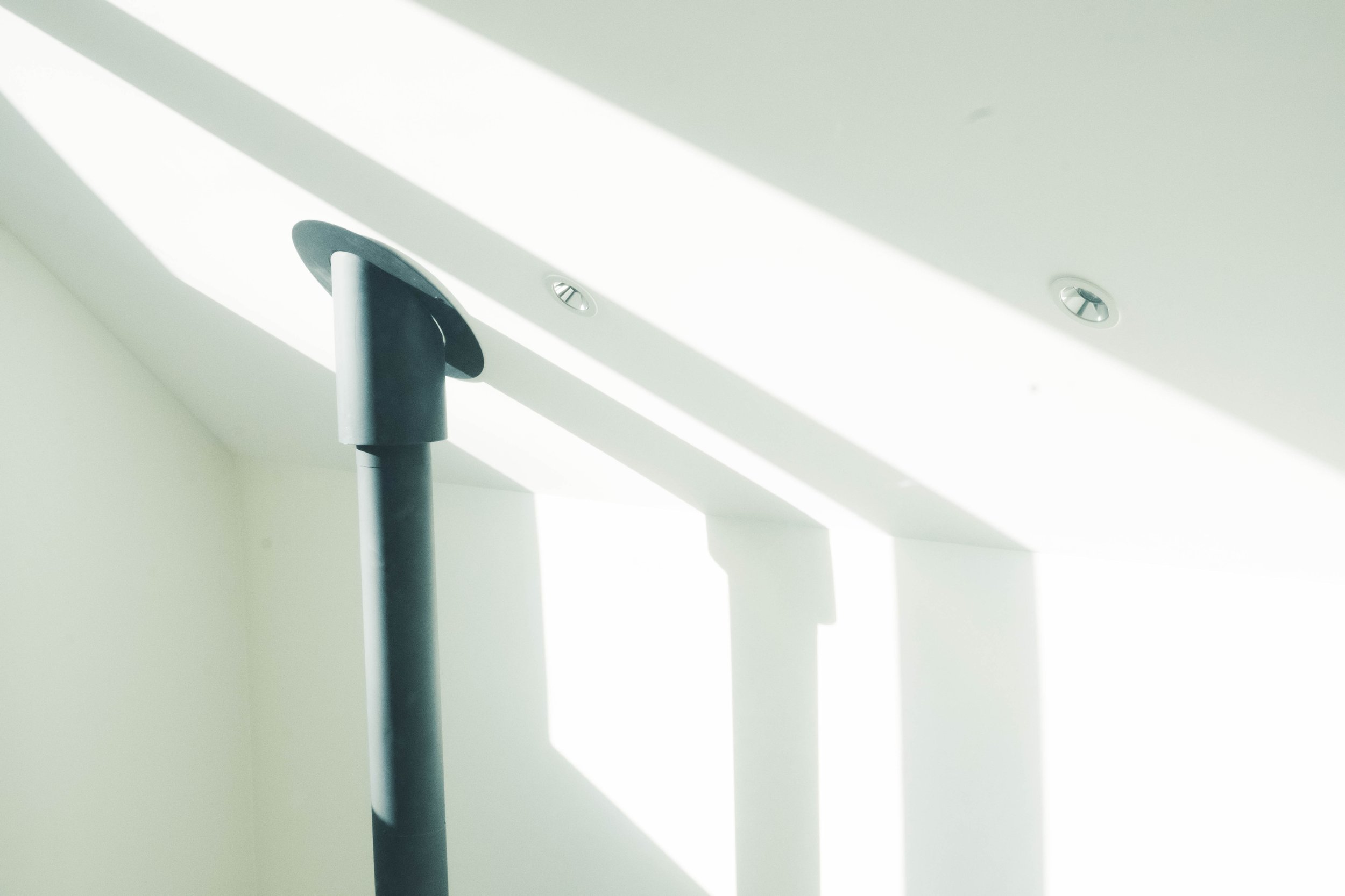 Close-up of a black metal handrail mounted on a white wall near a staircase, illuminated by sunlight.