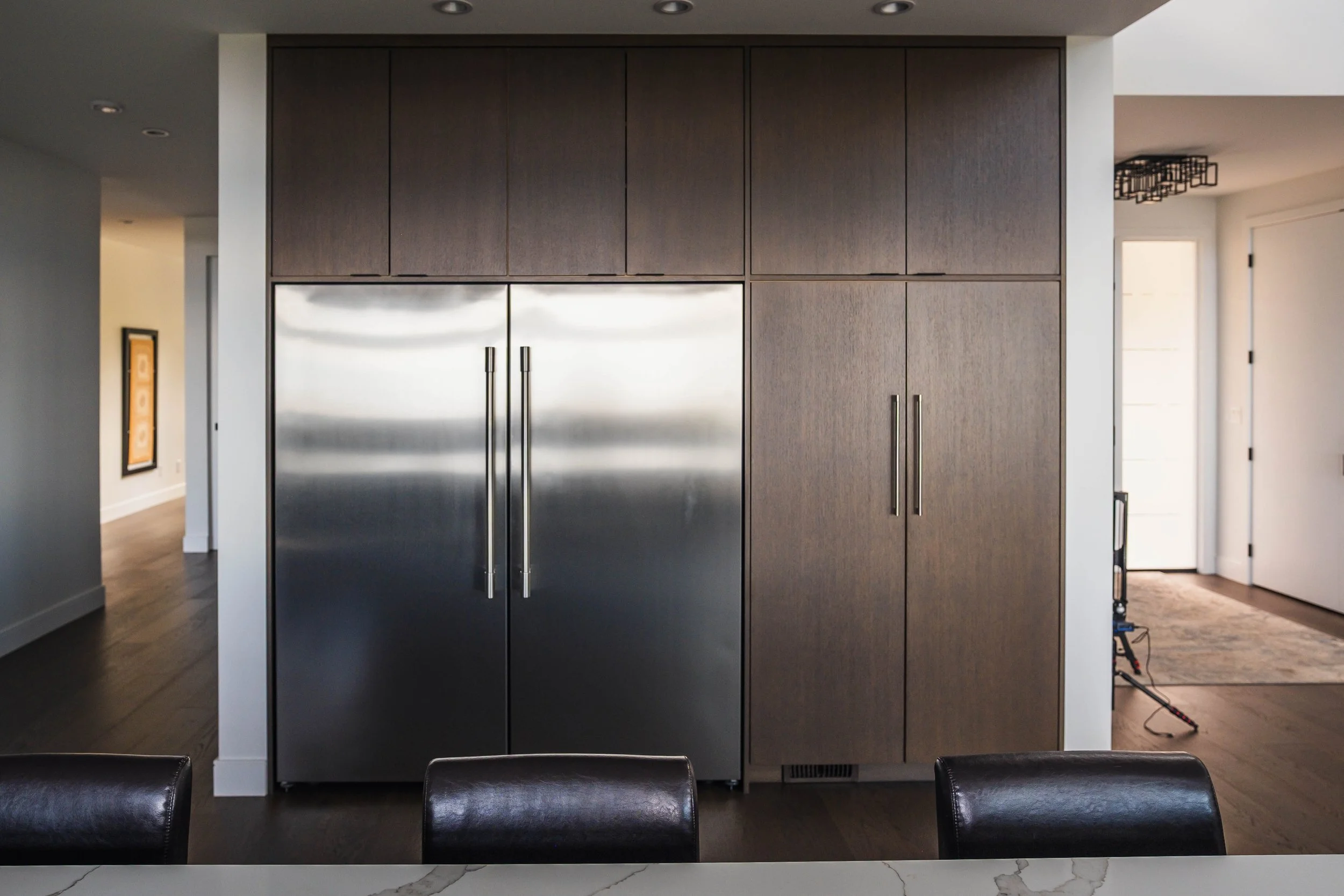 Modern kitchen with a built-in refrigerator, wooden cabinets above, and a marble countertop dining table with black chairs.