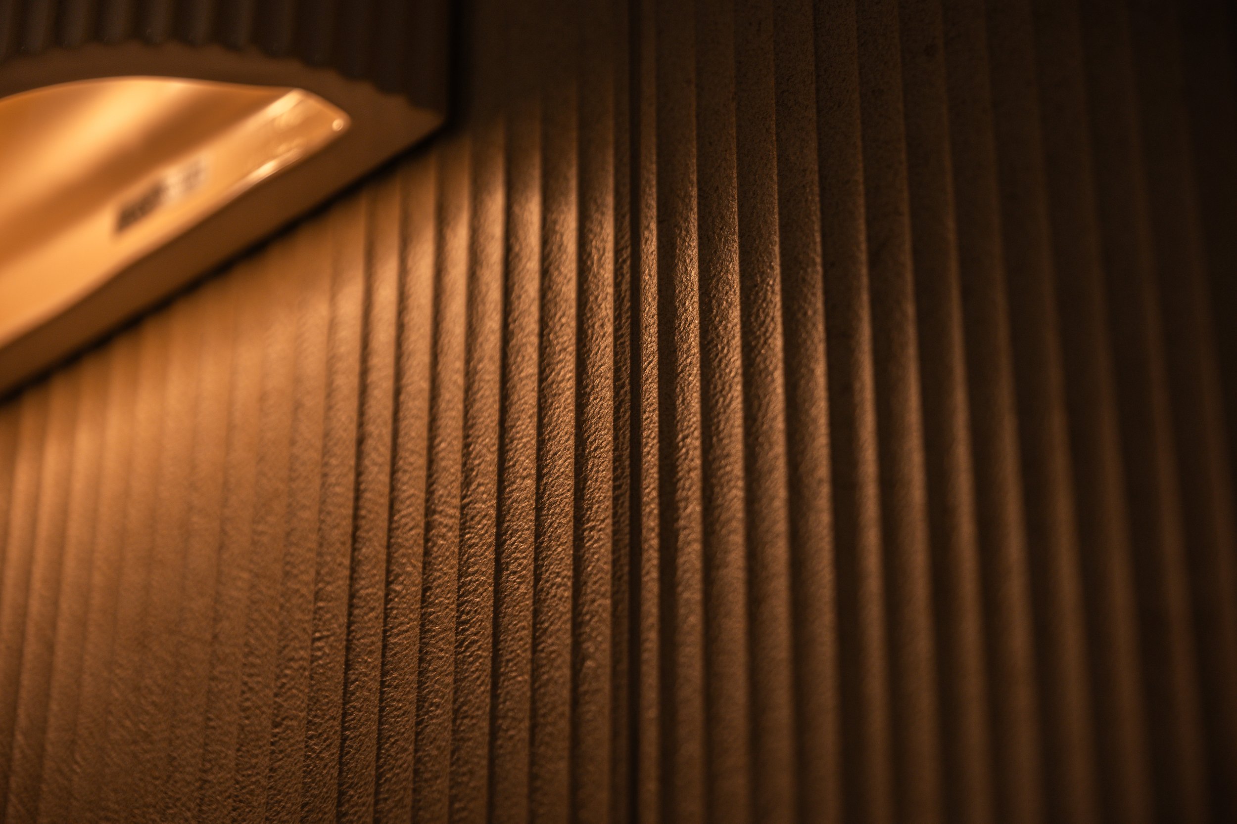 Close-up of a dark wooden surface with vertical grooves and a metallic object in the top left corner.