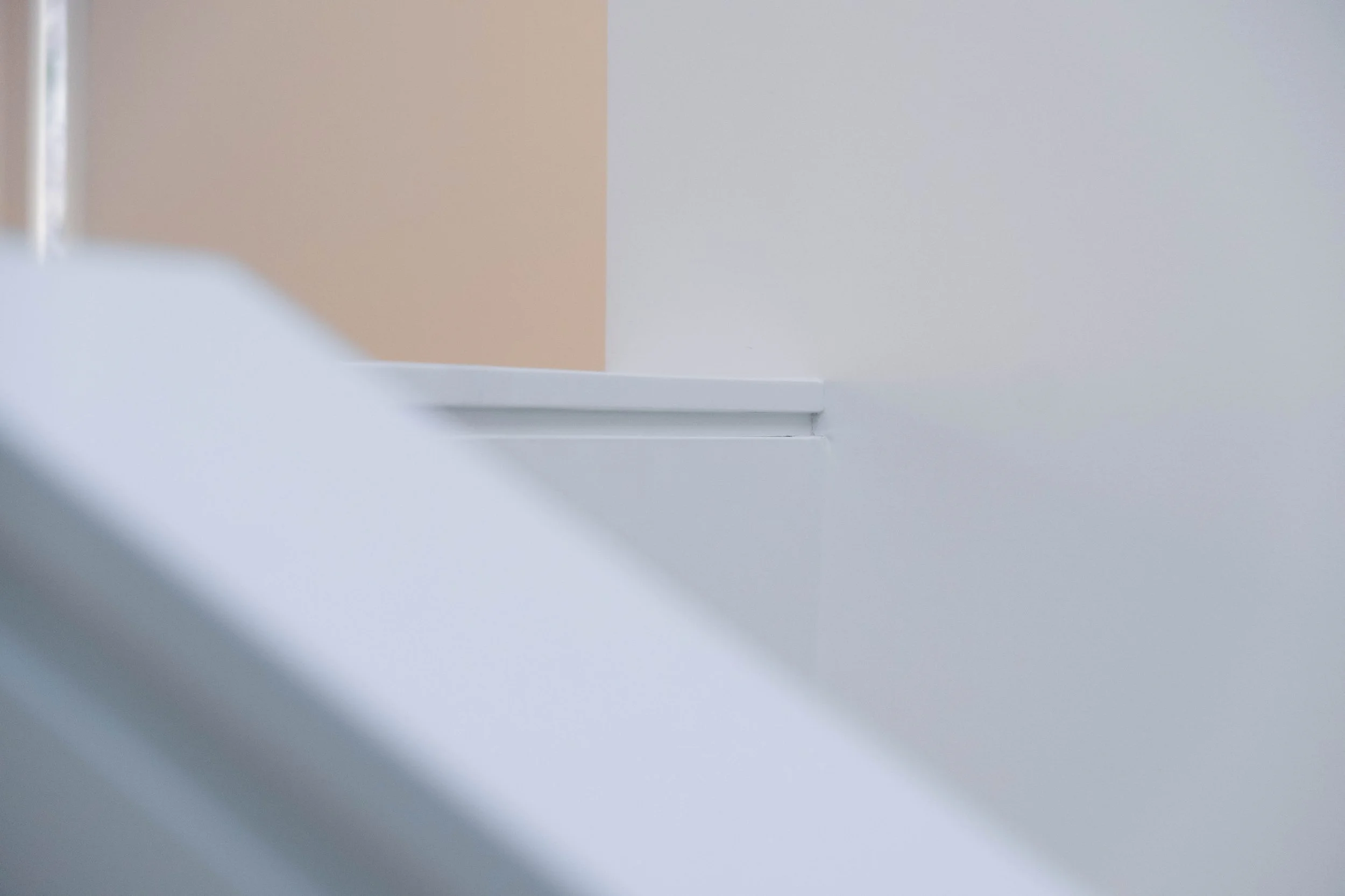 Close-up of a corner of a white and beige wall with a small white ledge or molding.